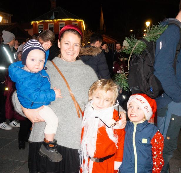 A woman standing with her 3 kids at a Christmas market. The kids are wearing santa outfits