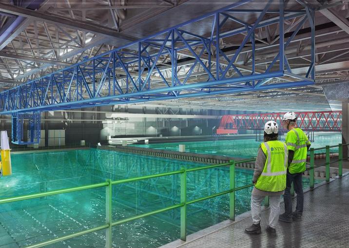 A water basin laboratory, related to maritime or offshore technology. The image features a large, industrial space with a water basin, for testing vessels and marine equipment, with workers in safety gear overseeing the operation. There's a focus on both practical and technical aspects, such as overhead cranes and a computer-controlled section.