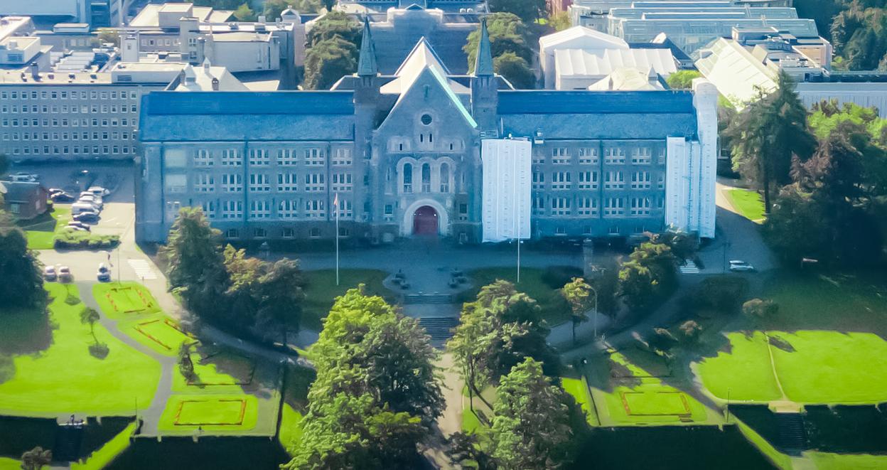 Aerial view of the NTNU Main Building in Trondheim, Norway, surrounded by lush green parks with the cityscape in the background.