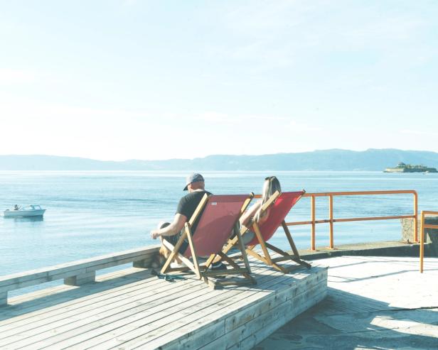 A couple chilling in sun-chairs at the pier, looking out over the sea. You can see the tiny island "Munkholmen" in the distance.