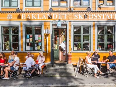 People hanging out outside of a restaurant on a beautiful summer day. You can see the shades from the trees close by on the restaurants yellow walls