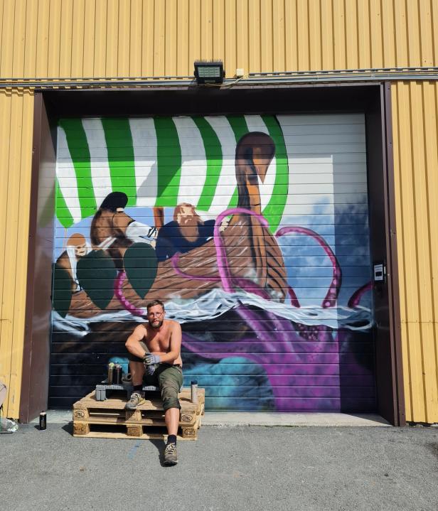 A shirtless man sitting in front of a very cool graffiti-painting of a viking ship, encountering a purple octopus