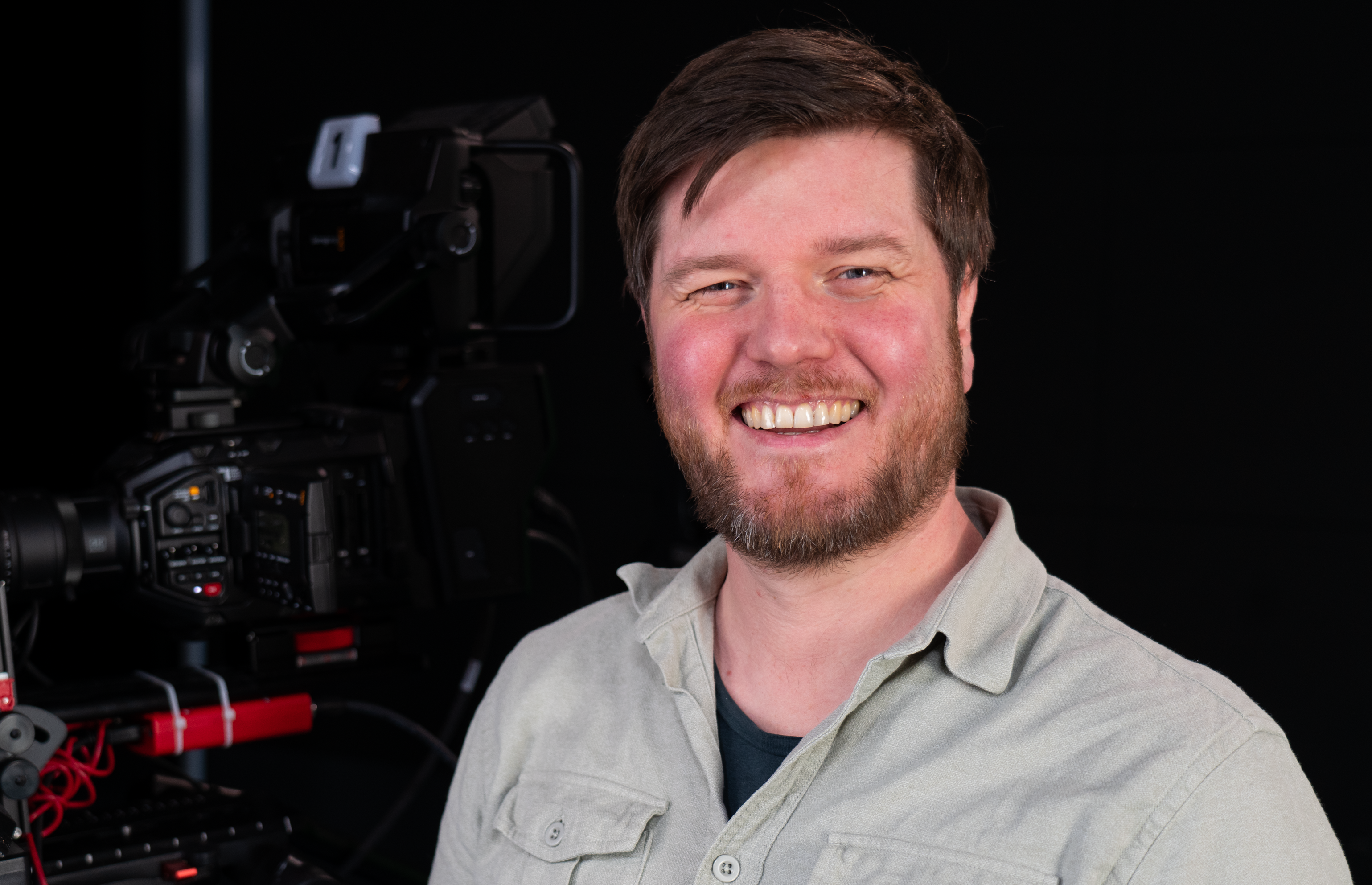 This is a photo of a person smiling, standing in front of a camera setup, possibly in a studio setting.