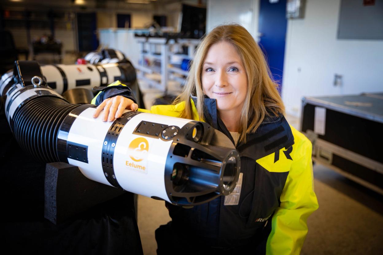 A woman standing next to a eel-like robot. 