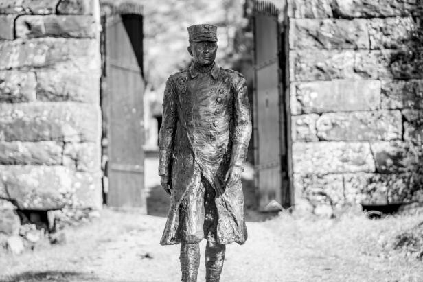 A statue of an old Norwegian major, made of metal. The statue is standing in front of a gate