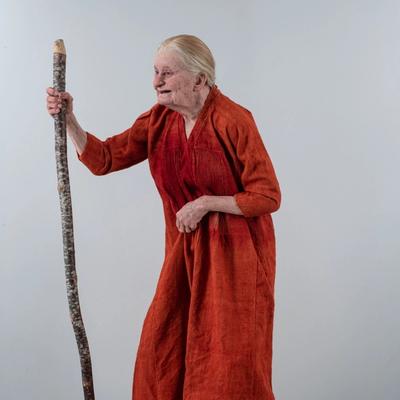 This is a remake of a medieval woman, depicted with an orange tunic and holding a walking stick, showcasing an aged appearance.