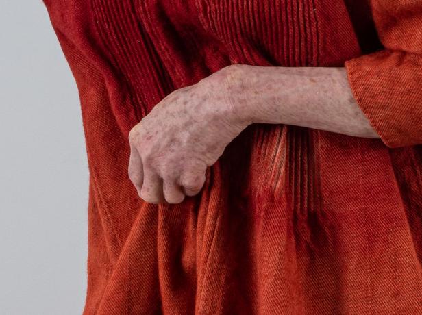 This is a remake of a medieval woman, depicted with an orange tunic and holding a walking stick, showcasing an aged appearance.