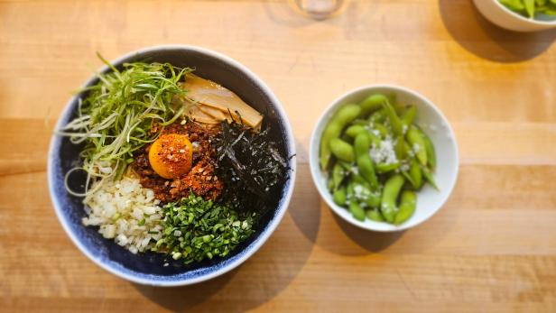 A bowl full of goodies: eggs, scallion, bamboo-sprouts and sea-weed topped with spices. Next to it is a bowl of edamame