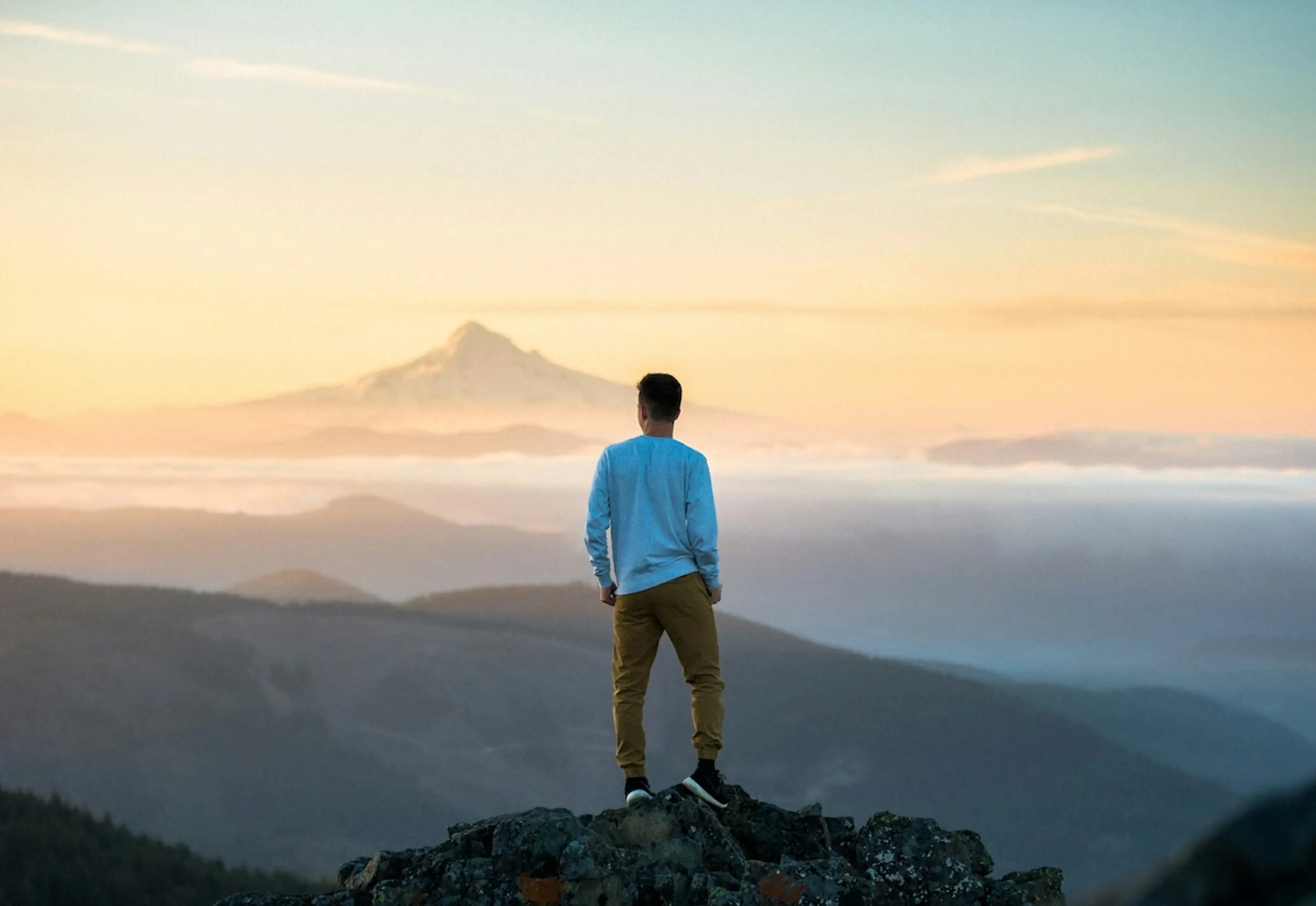 person standing on mountain peak looking into horizon