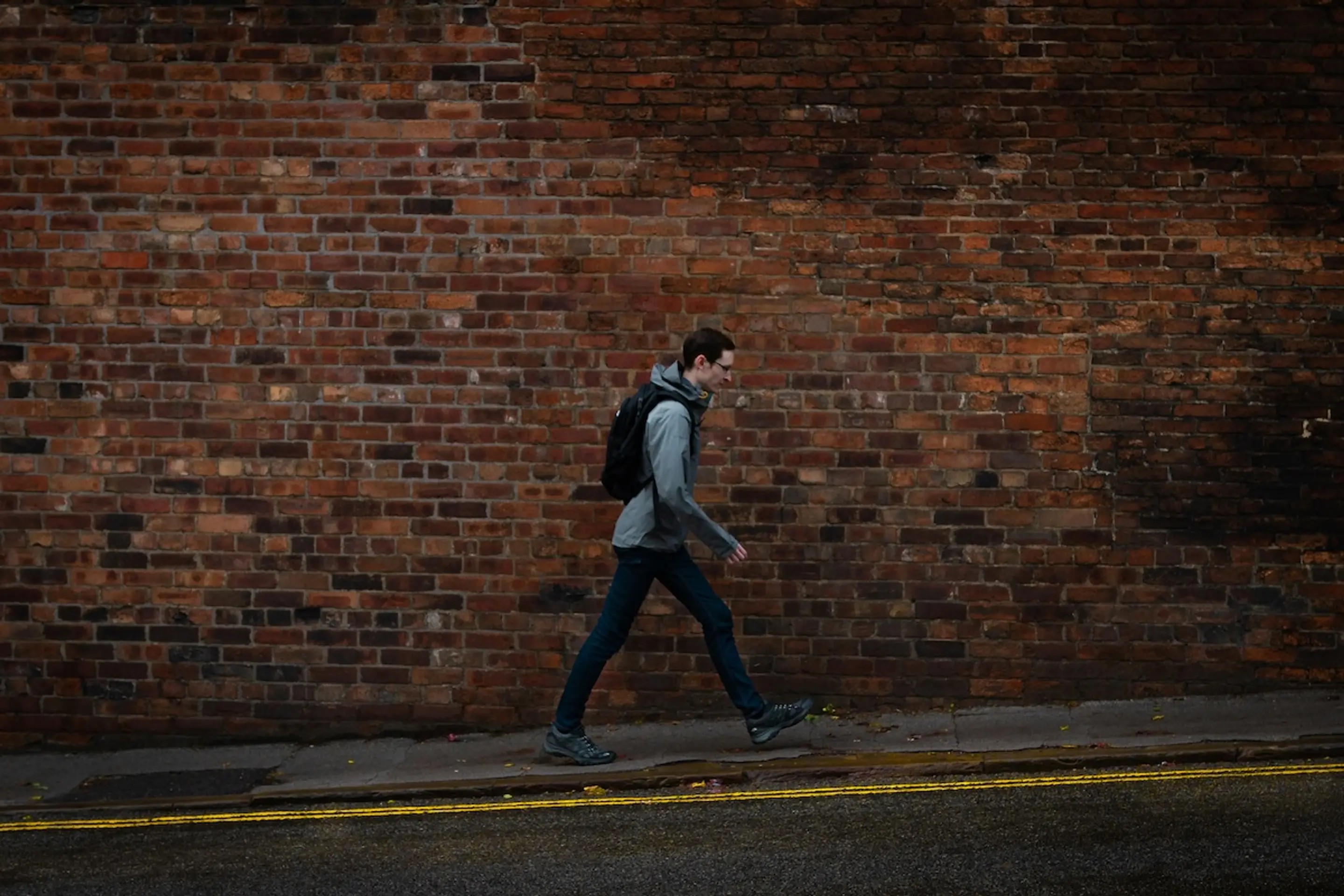 man with backpack walking on sidewalk next to brick building