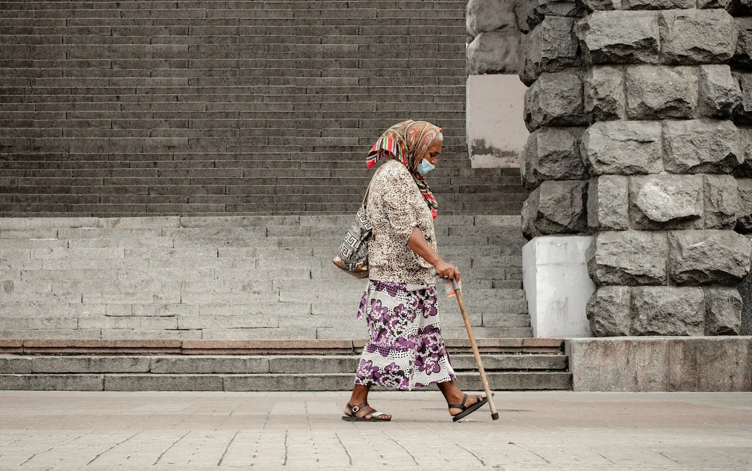 woman walking on street with cane and mask