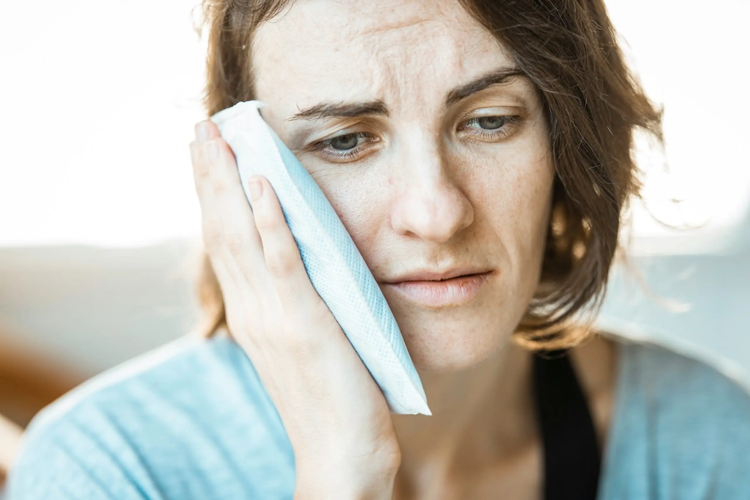 A woman with an ice pack on her cheek after wisdom teeth surgery