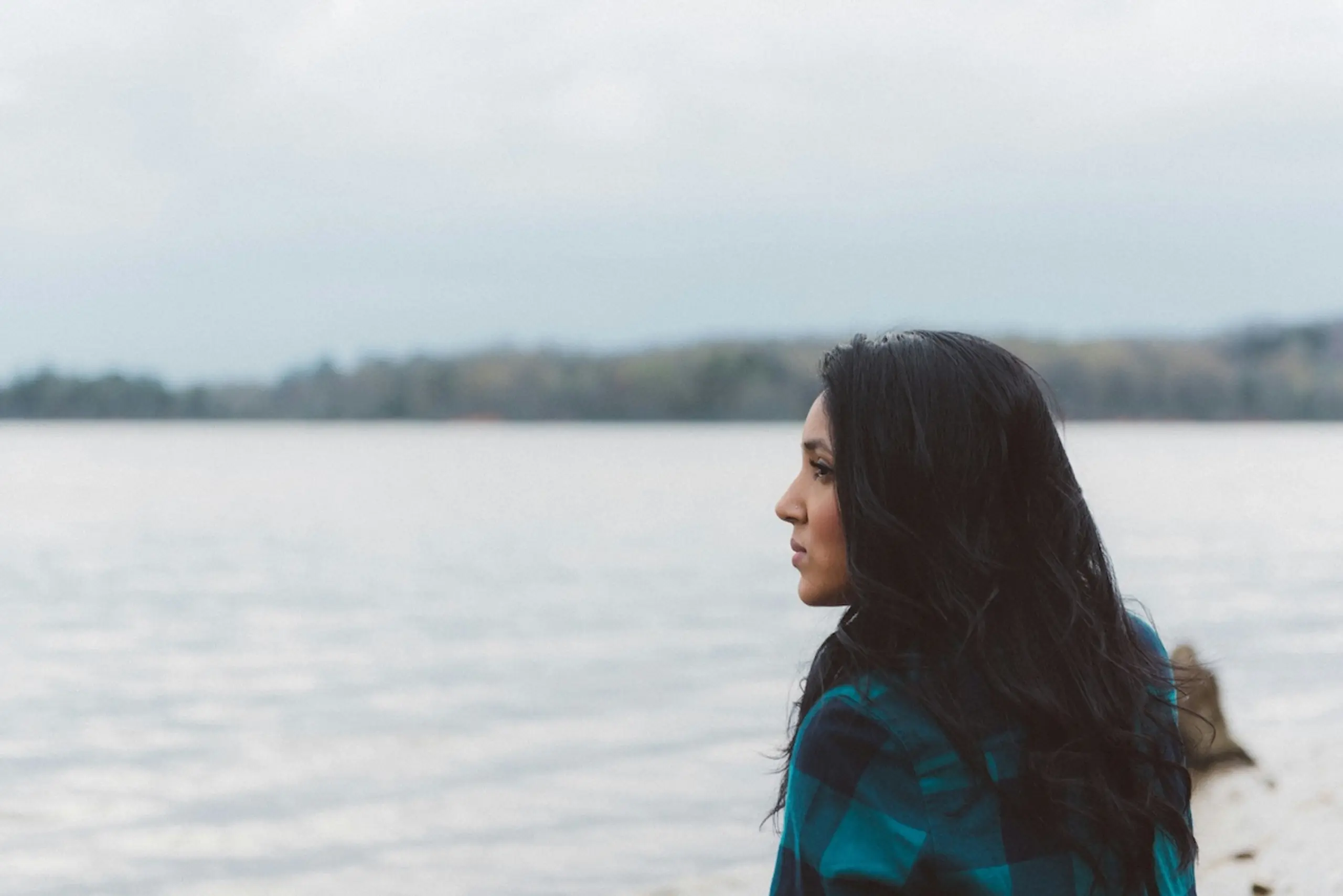 woman looking at lake with trees on the shore and cloudy sky