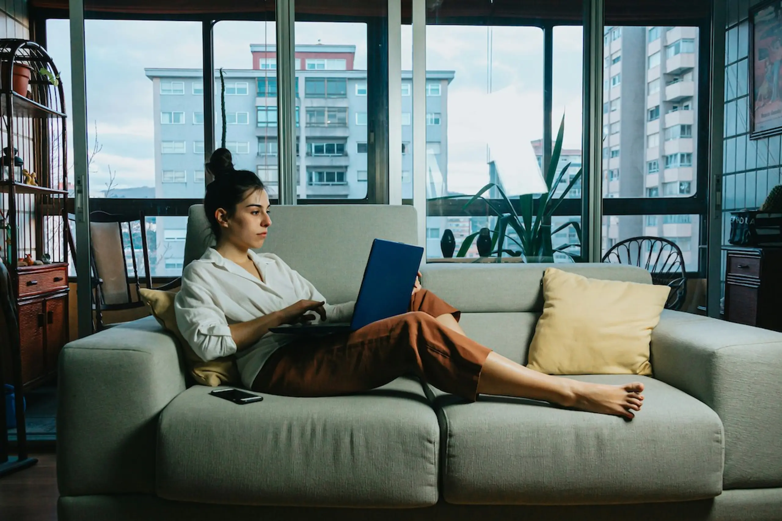 A woman at home on the couch reading on her laptop