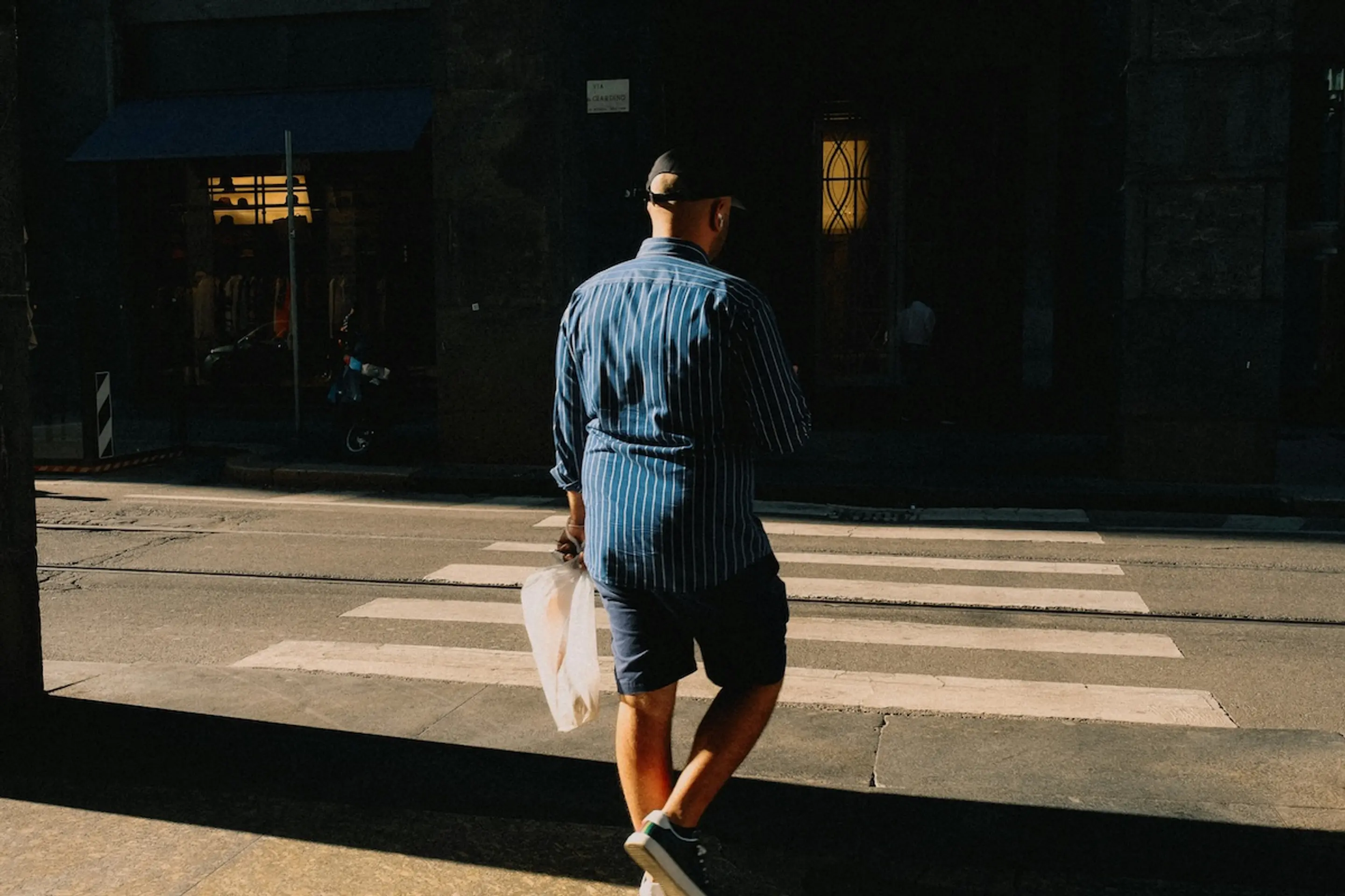 man walking across crosswalk carrying bas