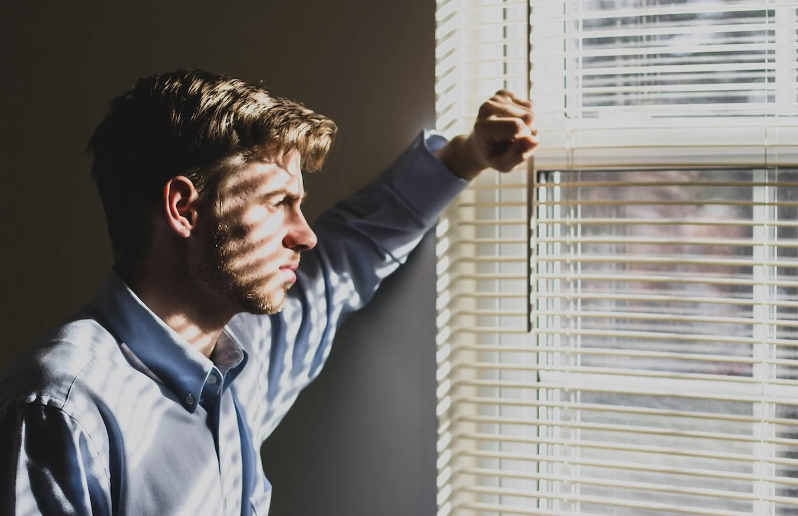 A concerned man looking out the window at home