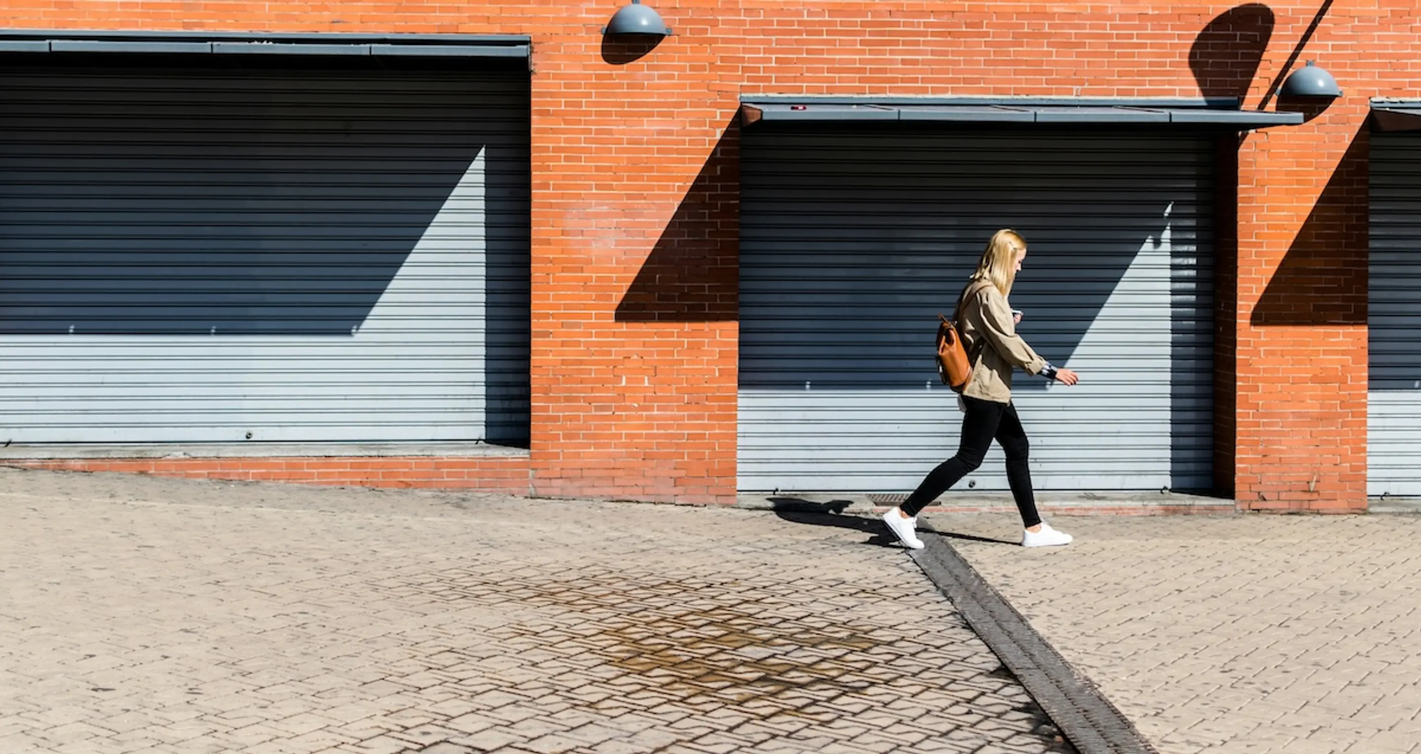 blonde woman walking on sidewalk next to garages