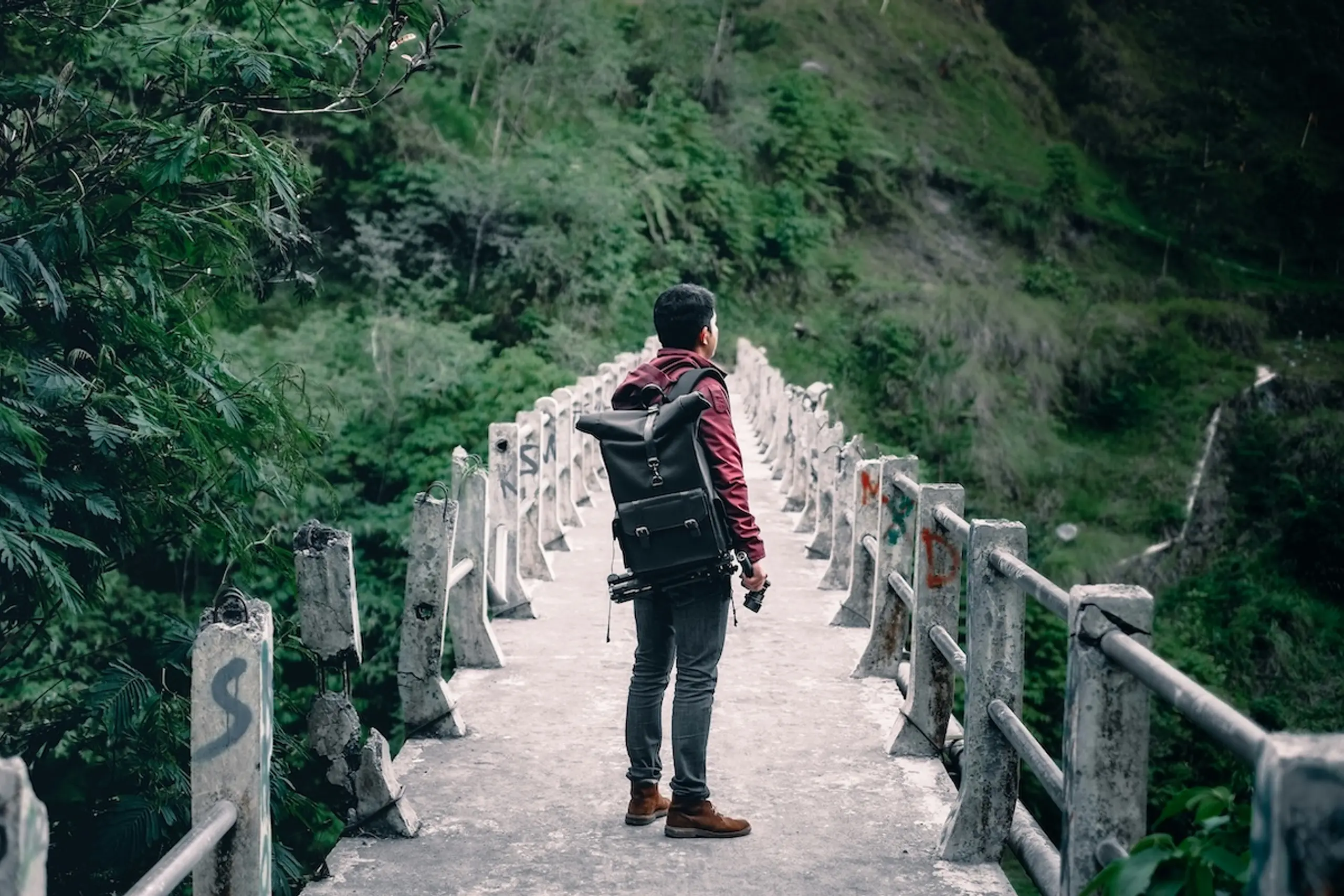 man standing on bridge in forest carrying black backpack