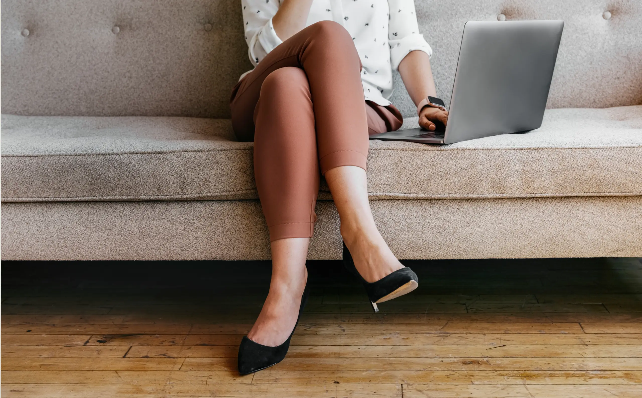 Woman with crossed legs sits on couch with laptop