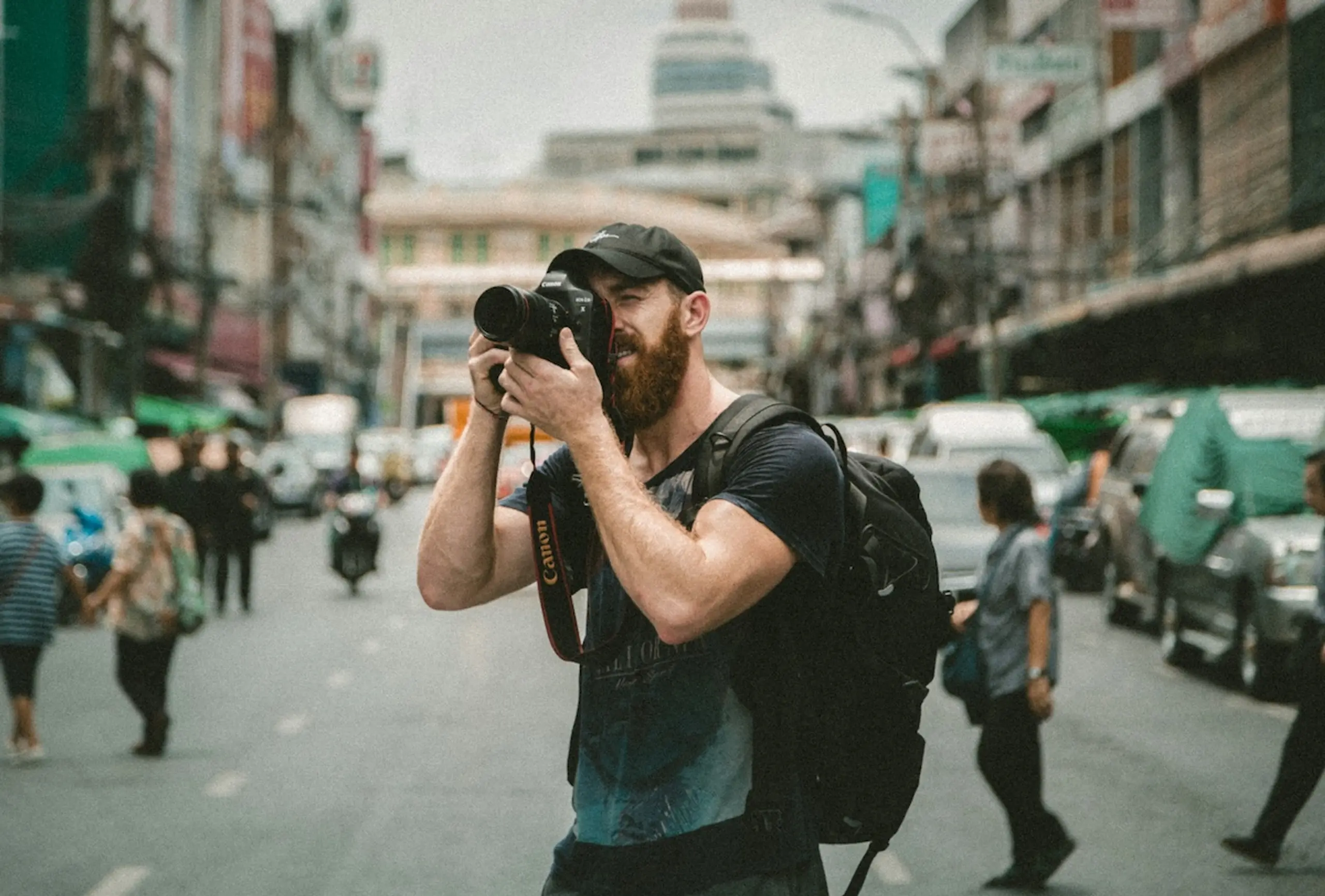 man with hat and beard taking photo in city street