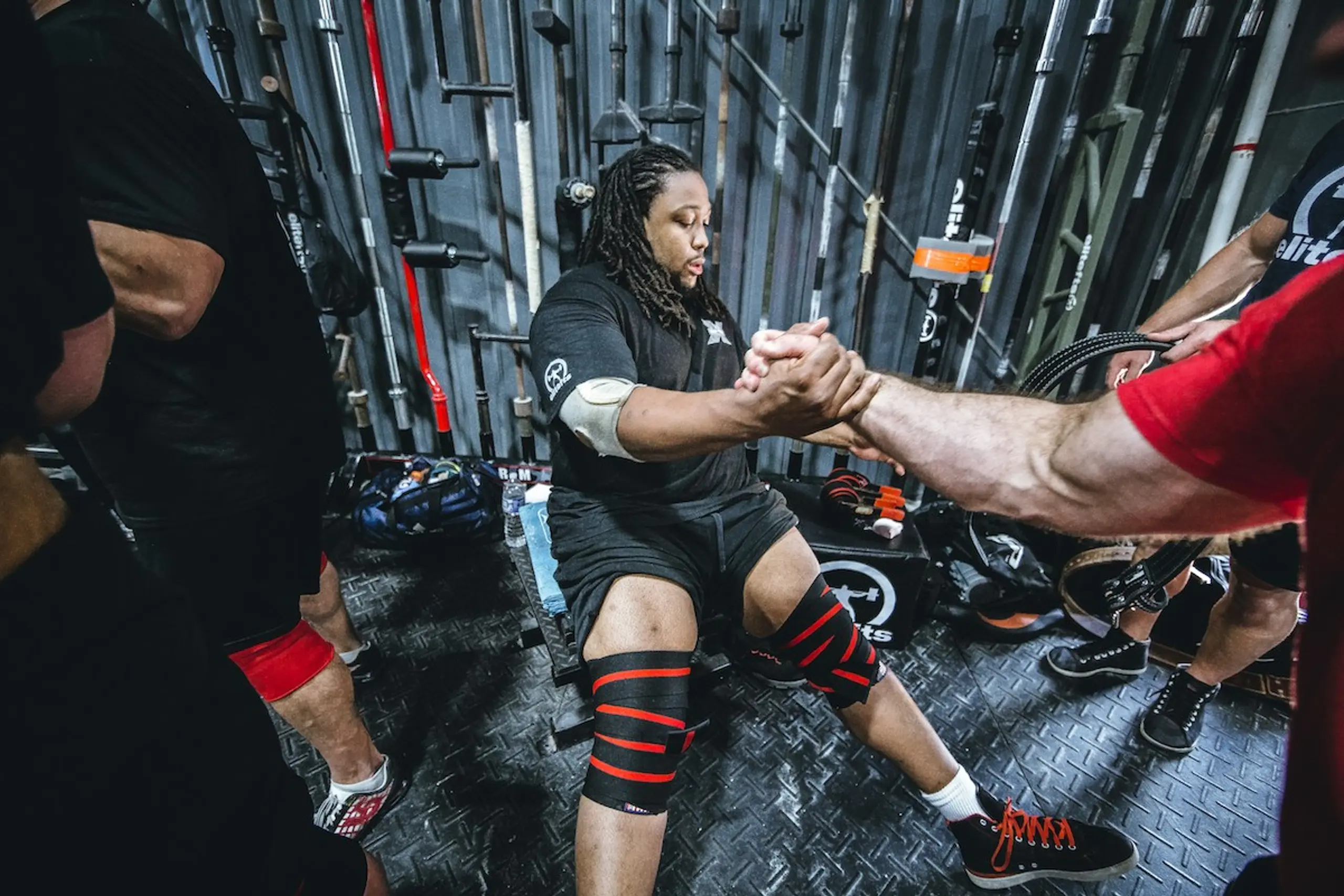 A guy with knee braces getting help standing up at the gym