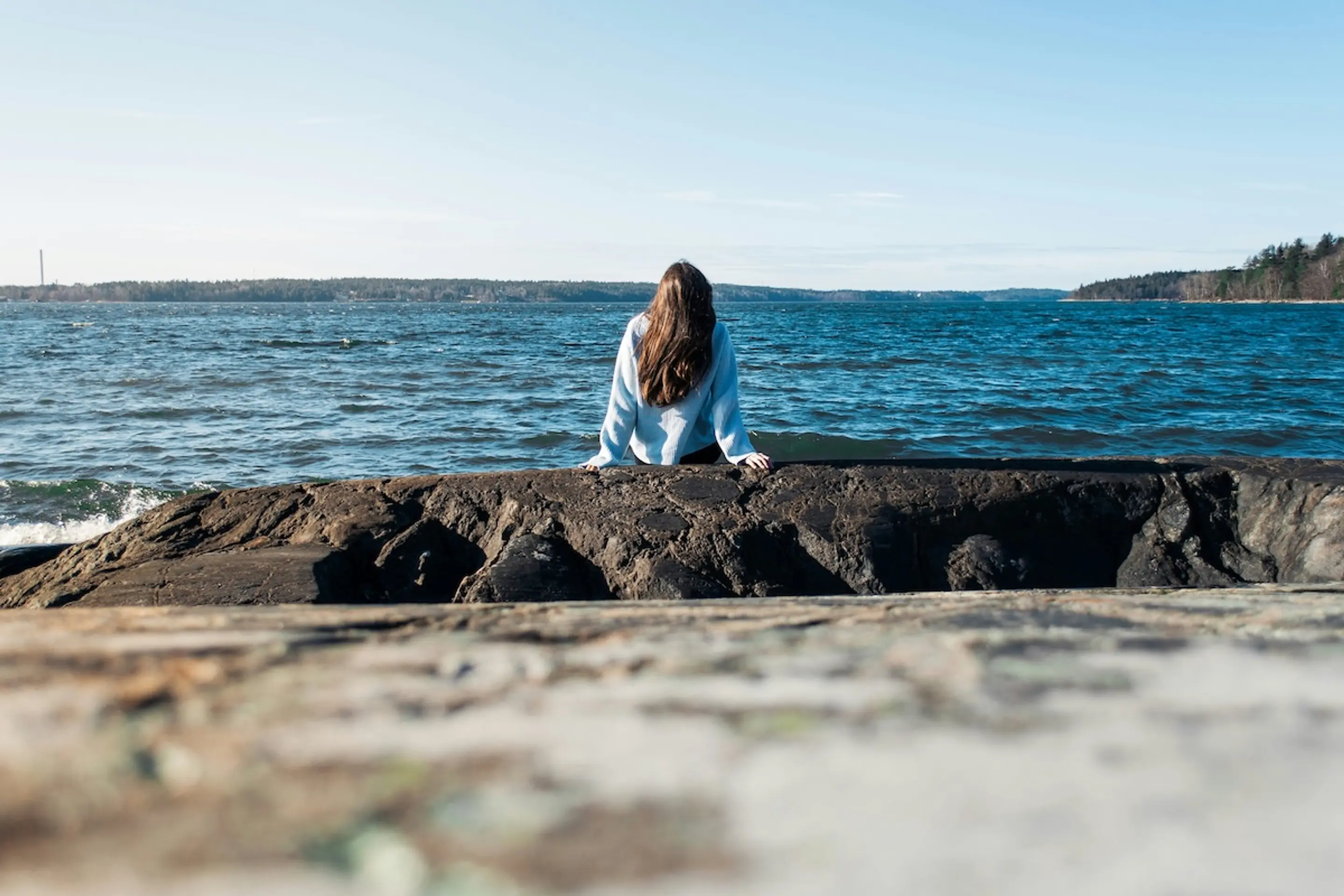 woman sitting on rocks at water's edge wearing sweater