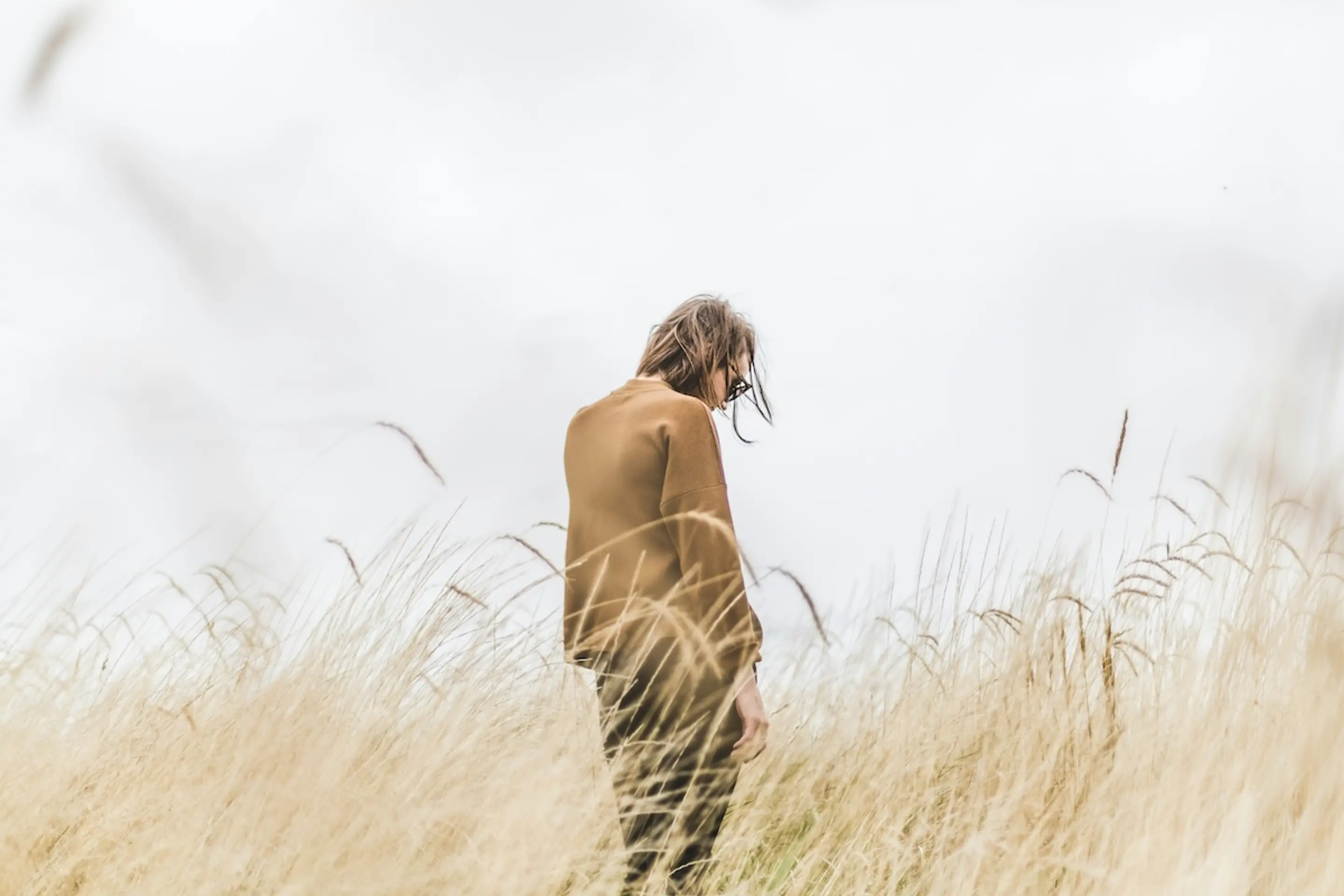 person looking down in wheat field wearing brown jacket