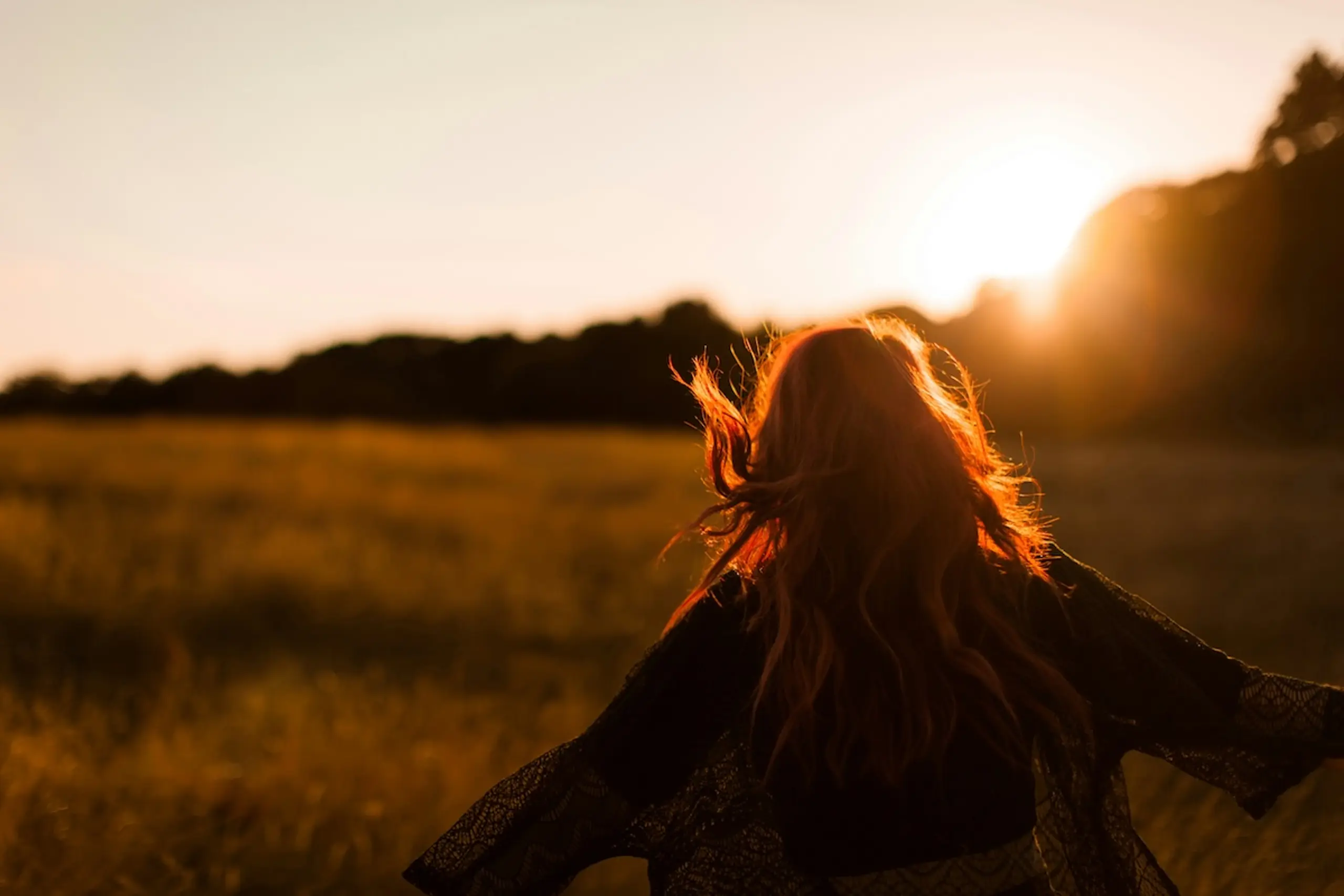 woman with open arms in field with sun and trees