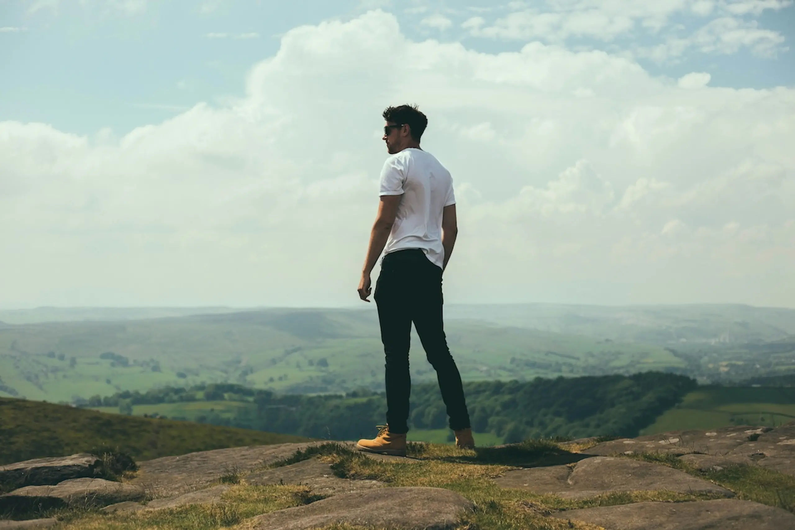 man in white shirt and black pants looking at cloudy, mountainous horizon