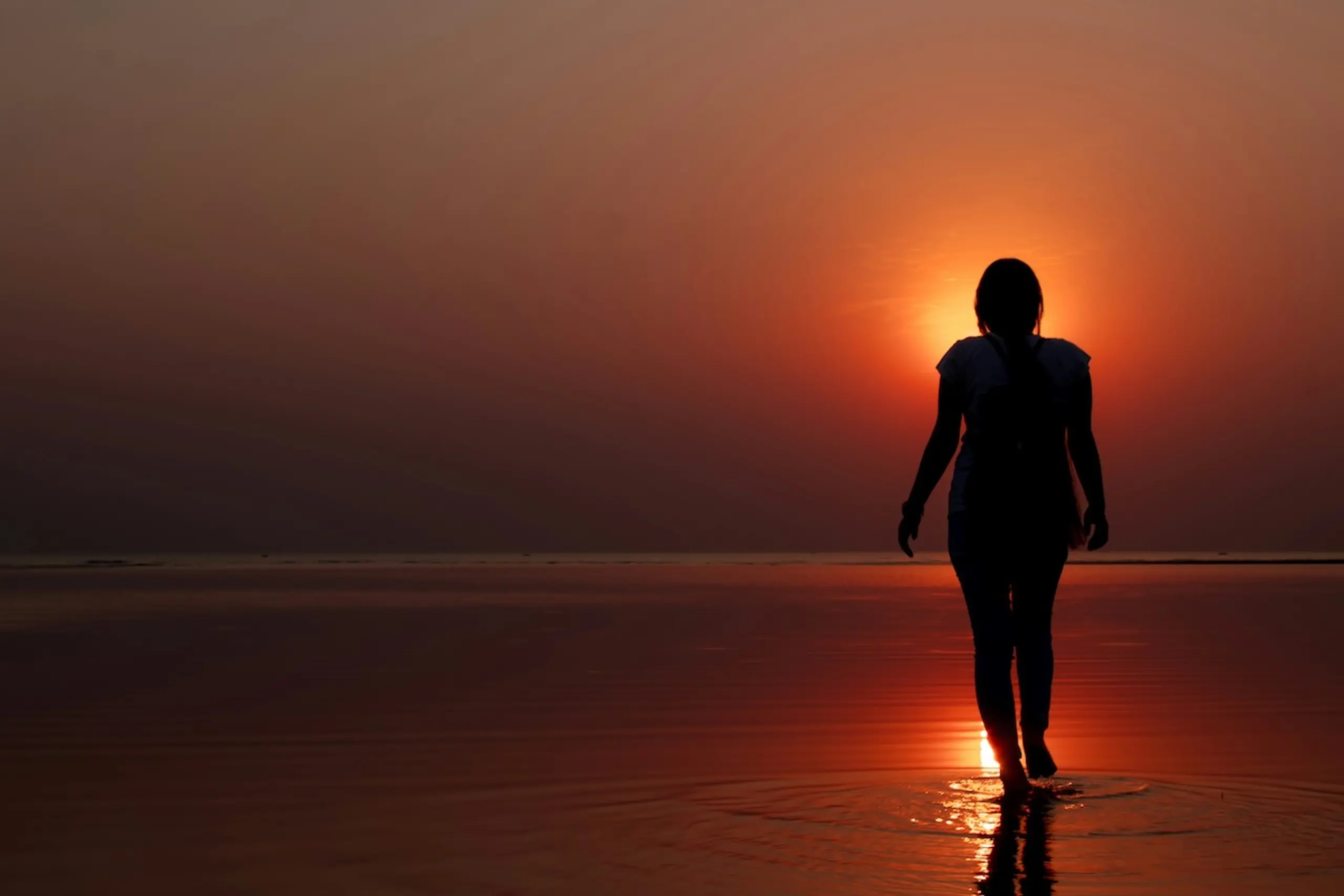 person walking in water towards sun