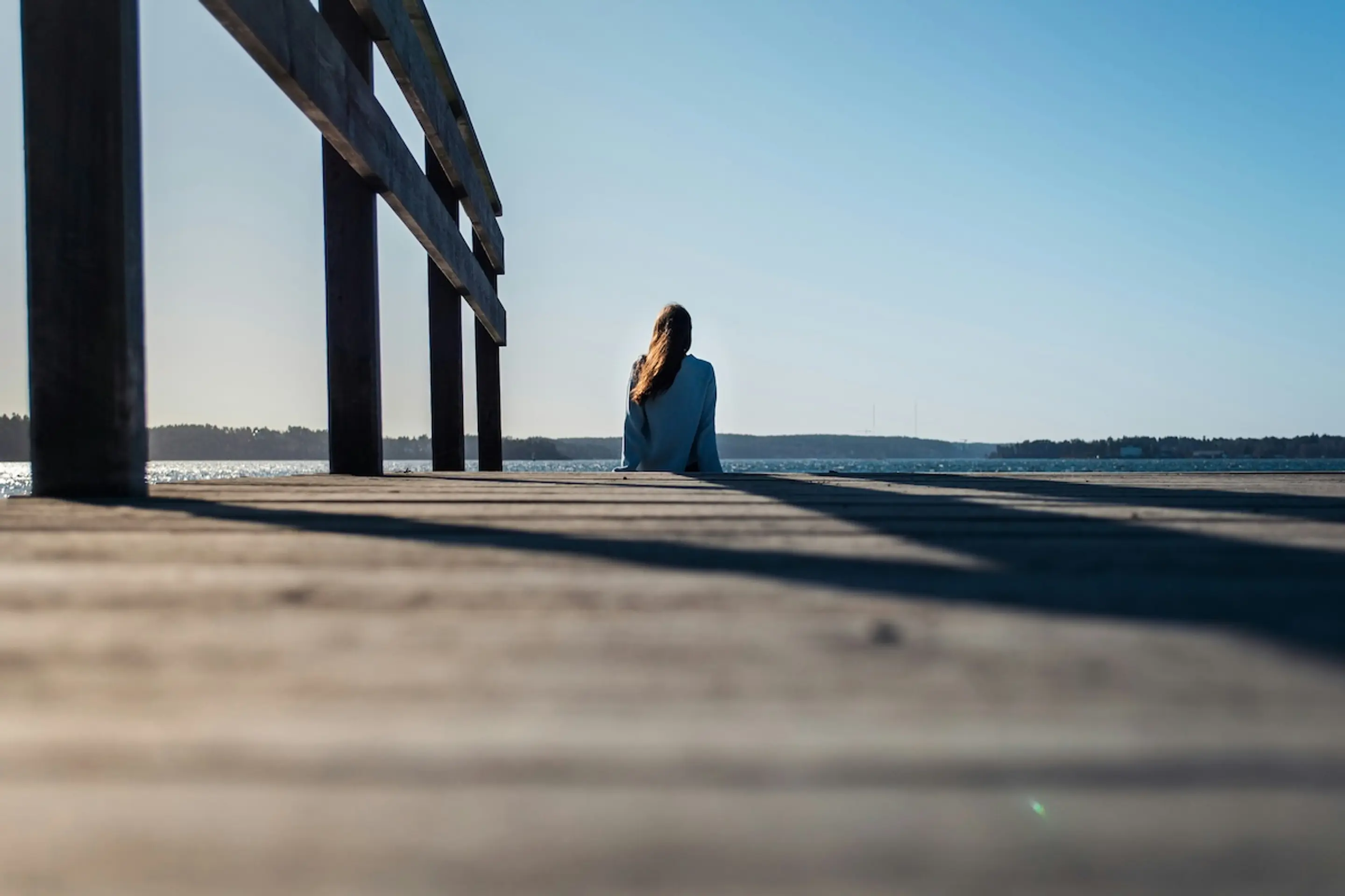 woman sitting at the end of a wooden dock on the water