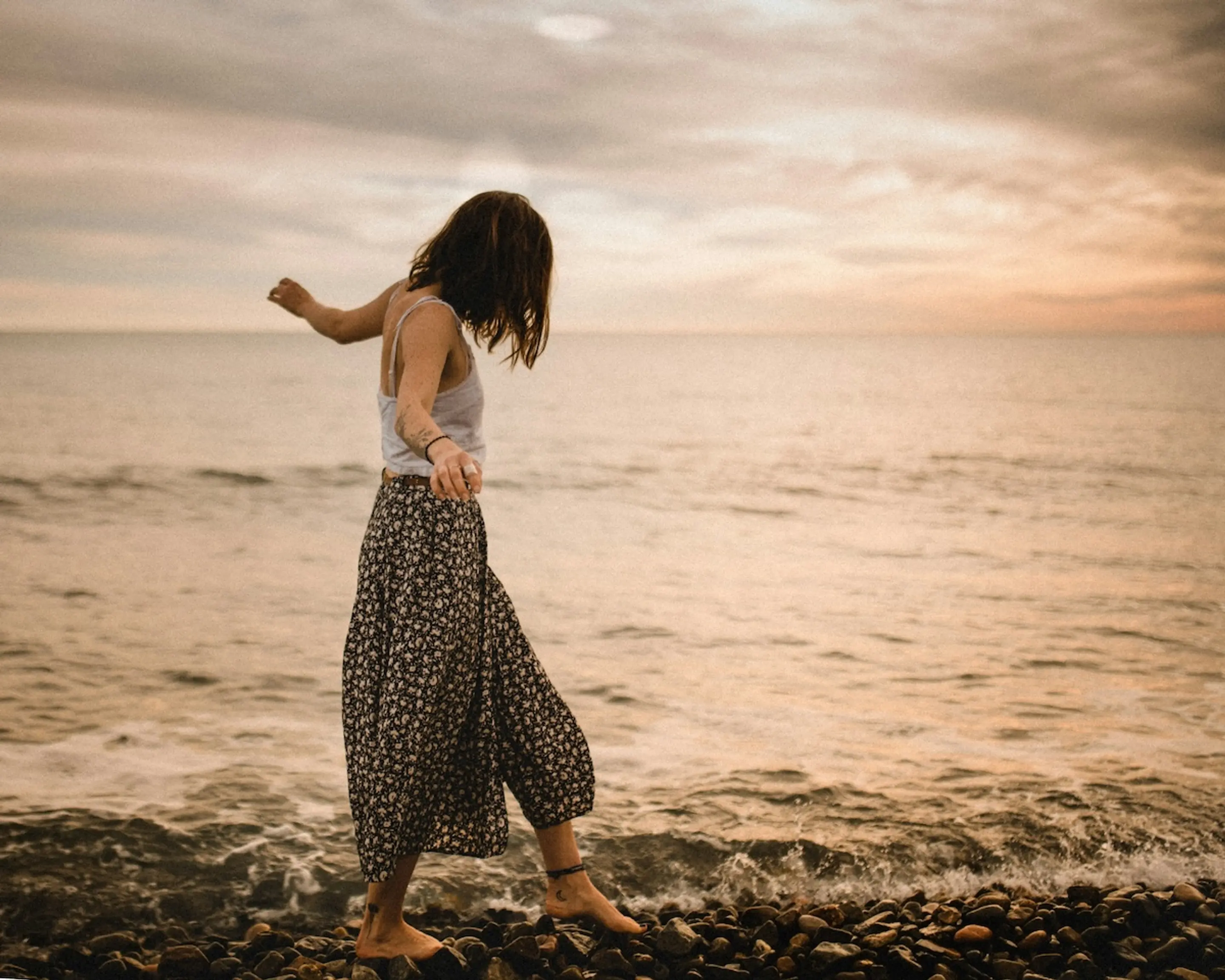woman wearing skirt walking at water's edge on rocks with a cloudy sky in the background