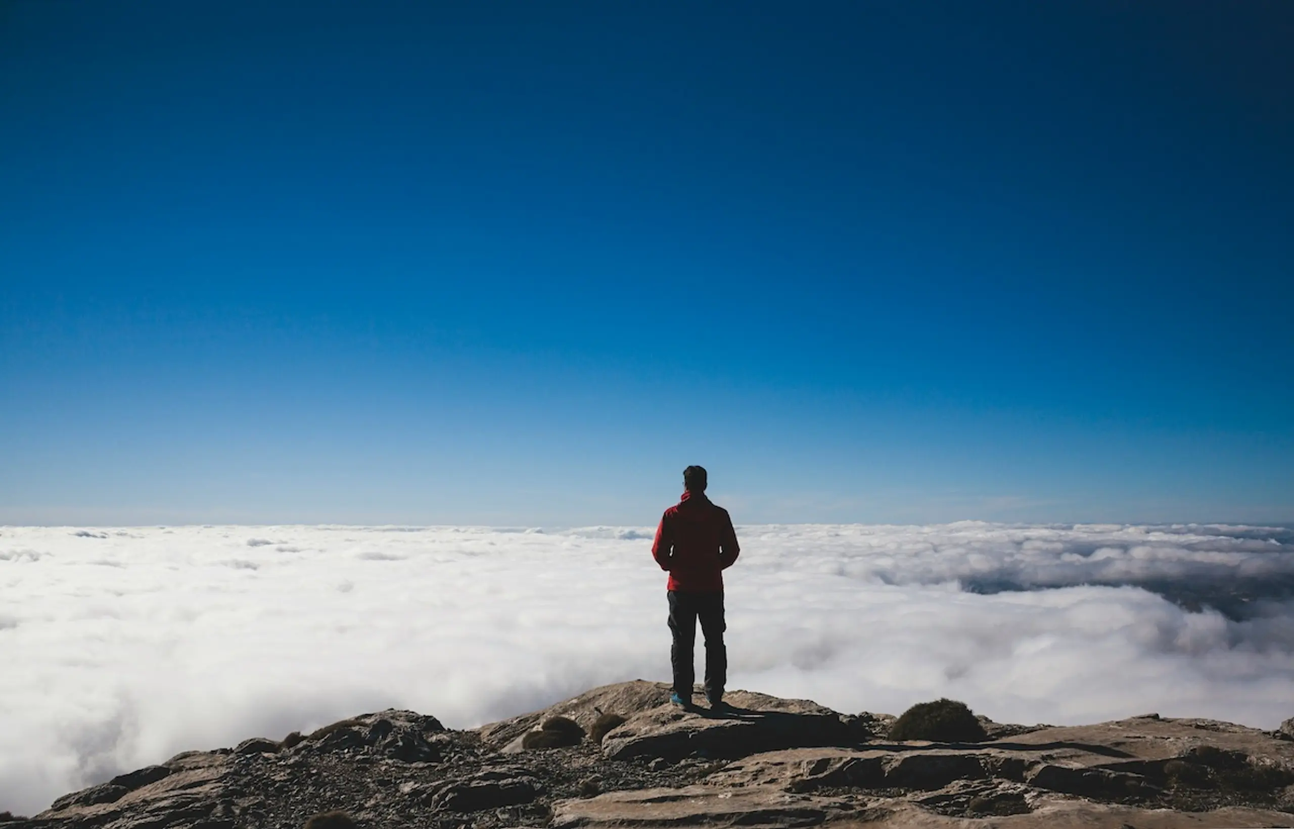 person overlooking clouds on mountain peak