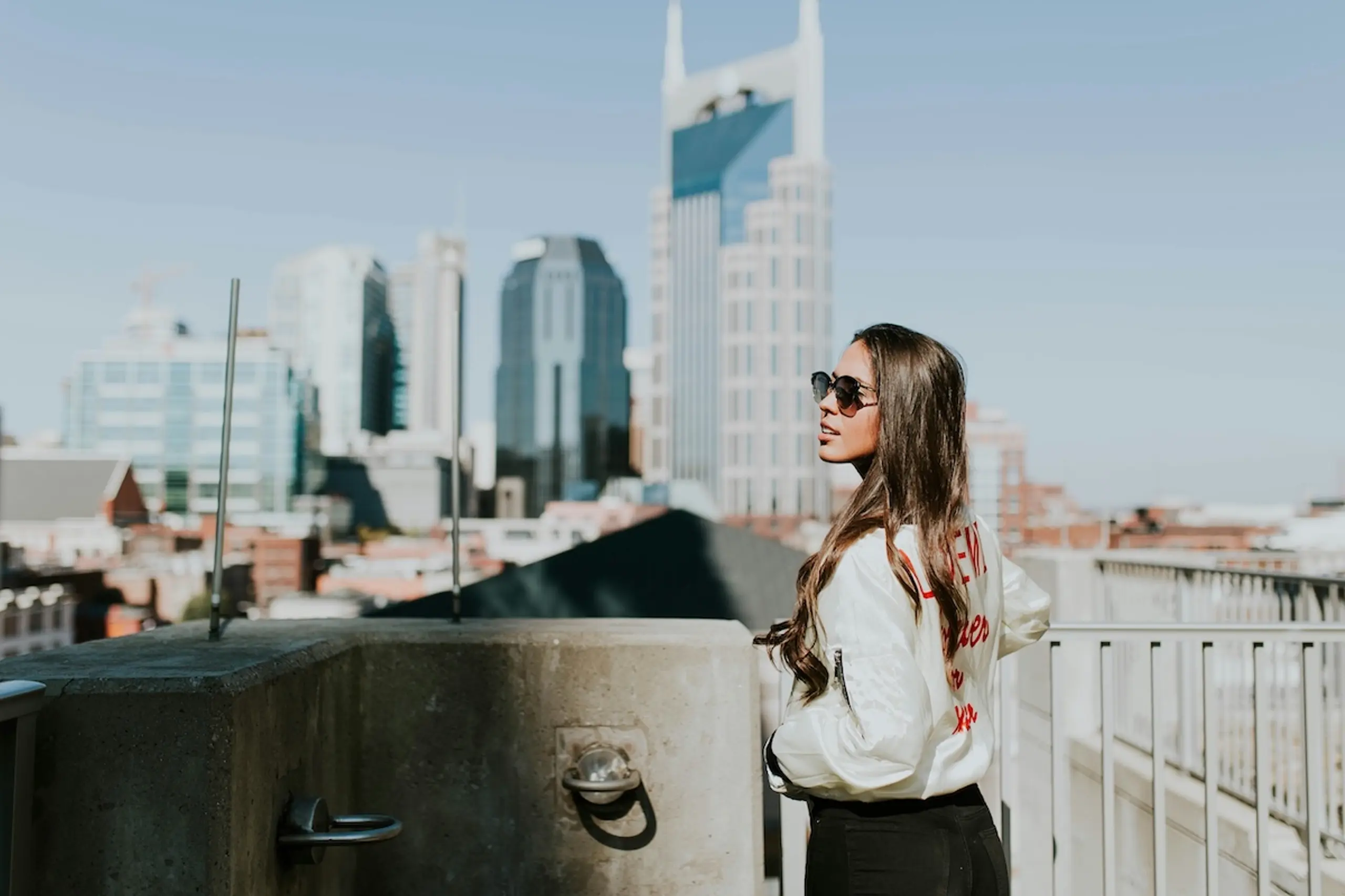 A woman wearing sunglasses on rooftop looking at buildings in city