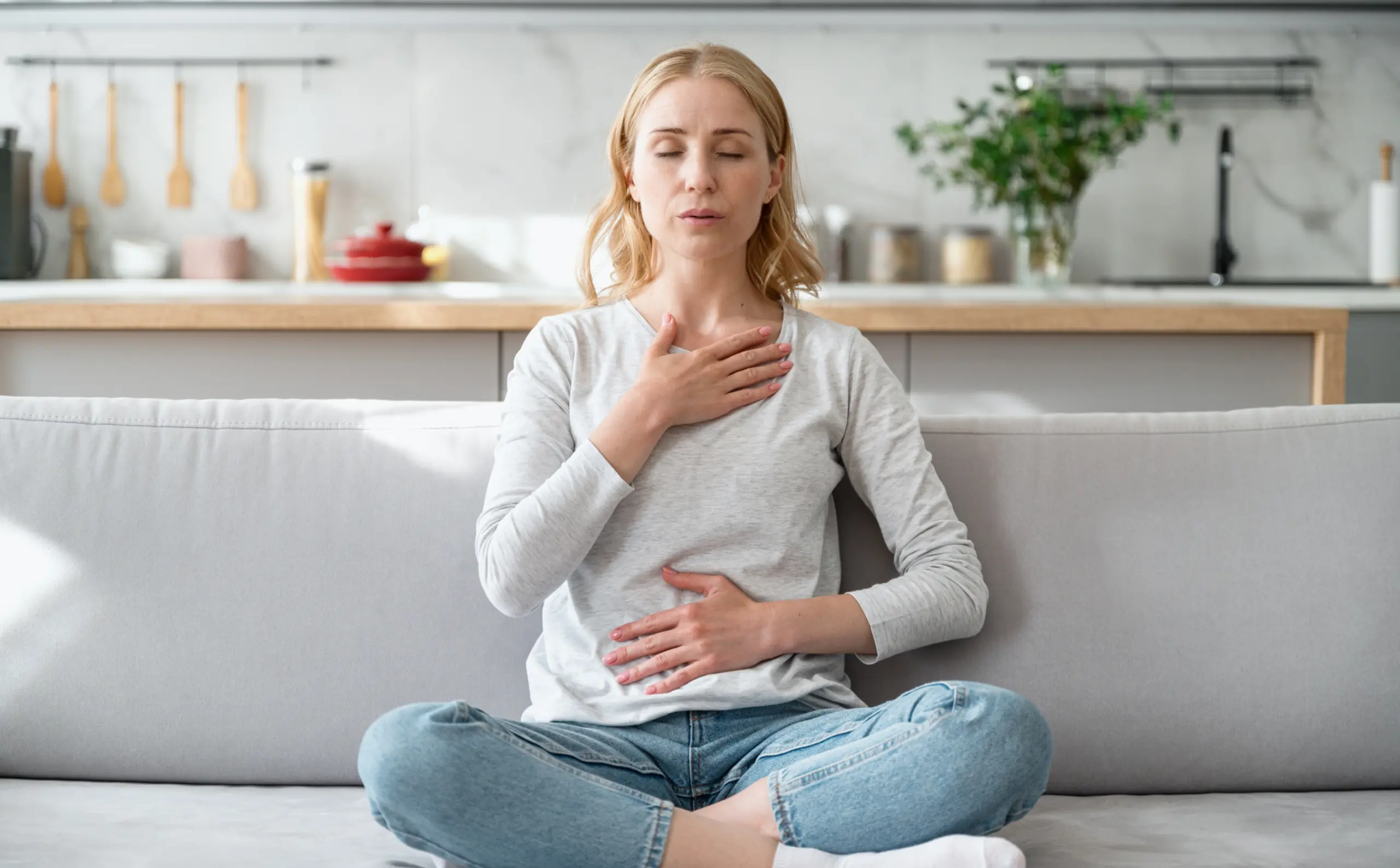 woman on couch breathing deeply with hands on heart and stomach