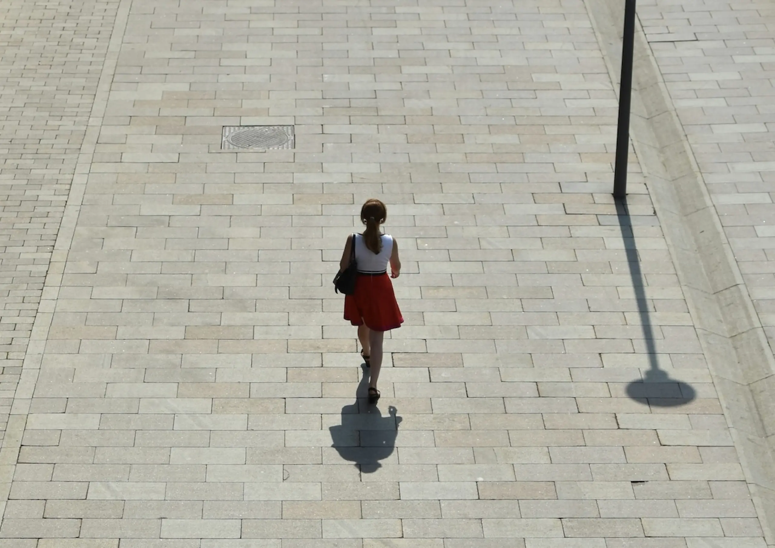 woman walking on sidewalk with lampost and shadows