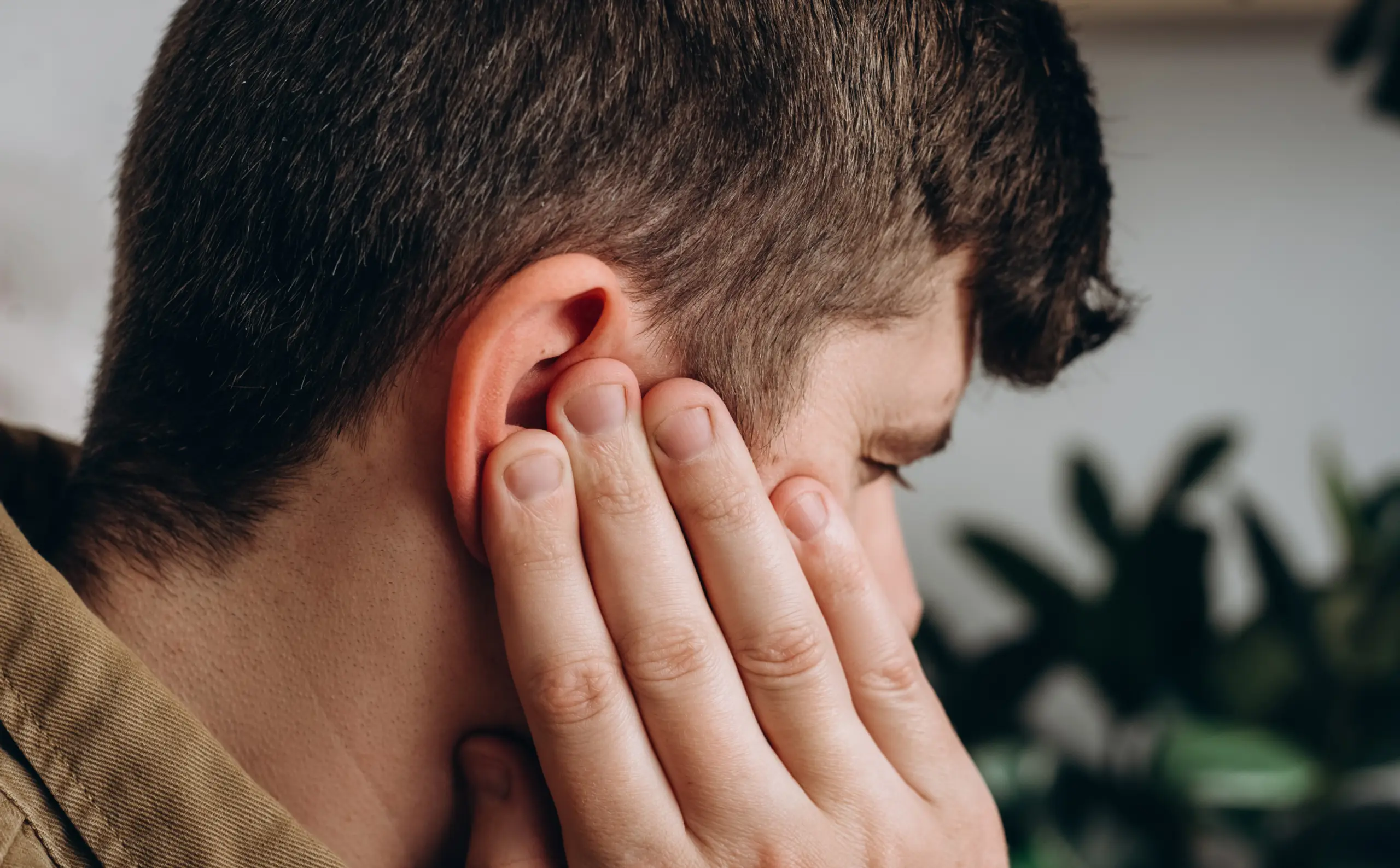Man presses hand against ear