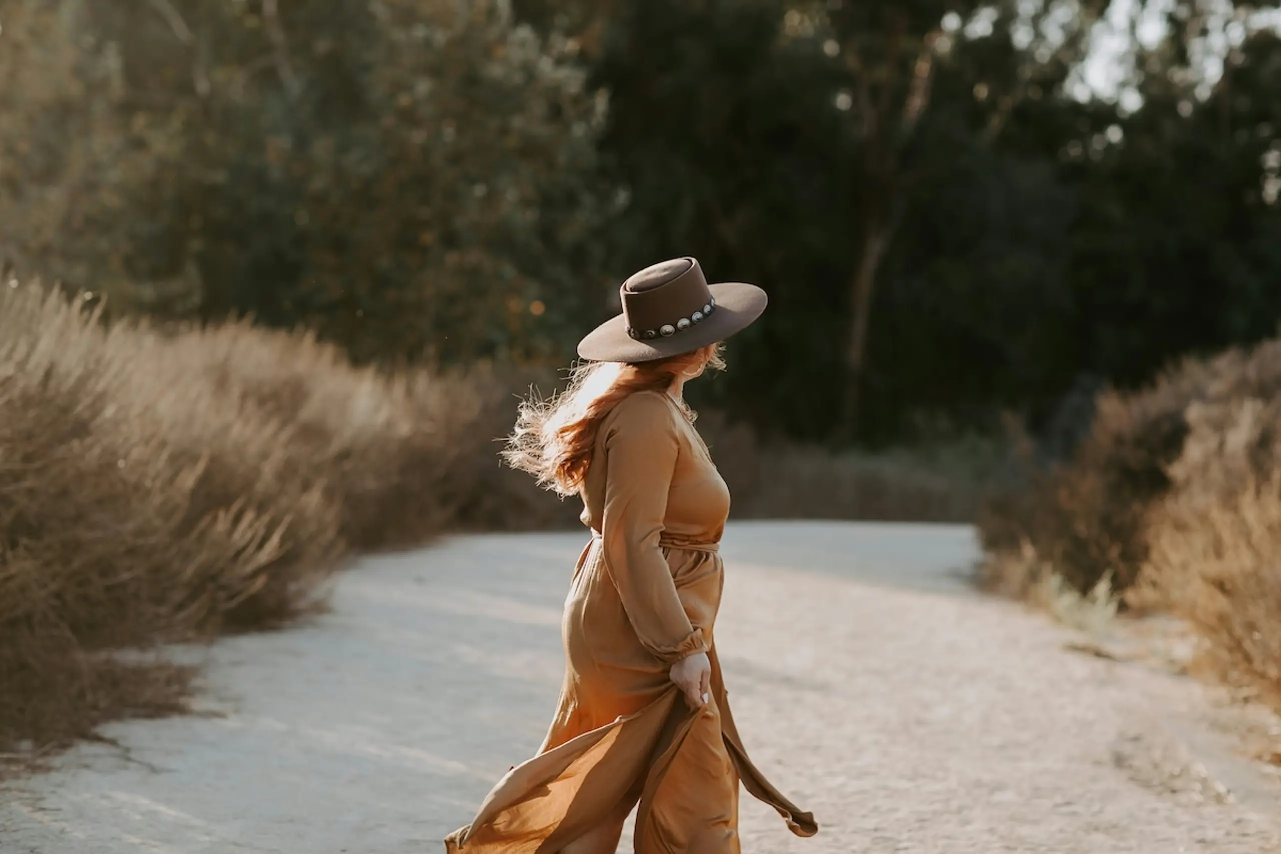 woman wearing hat and dress walking on sandy path