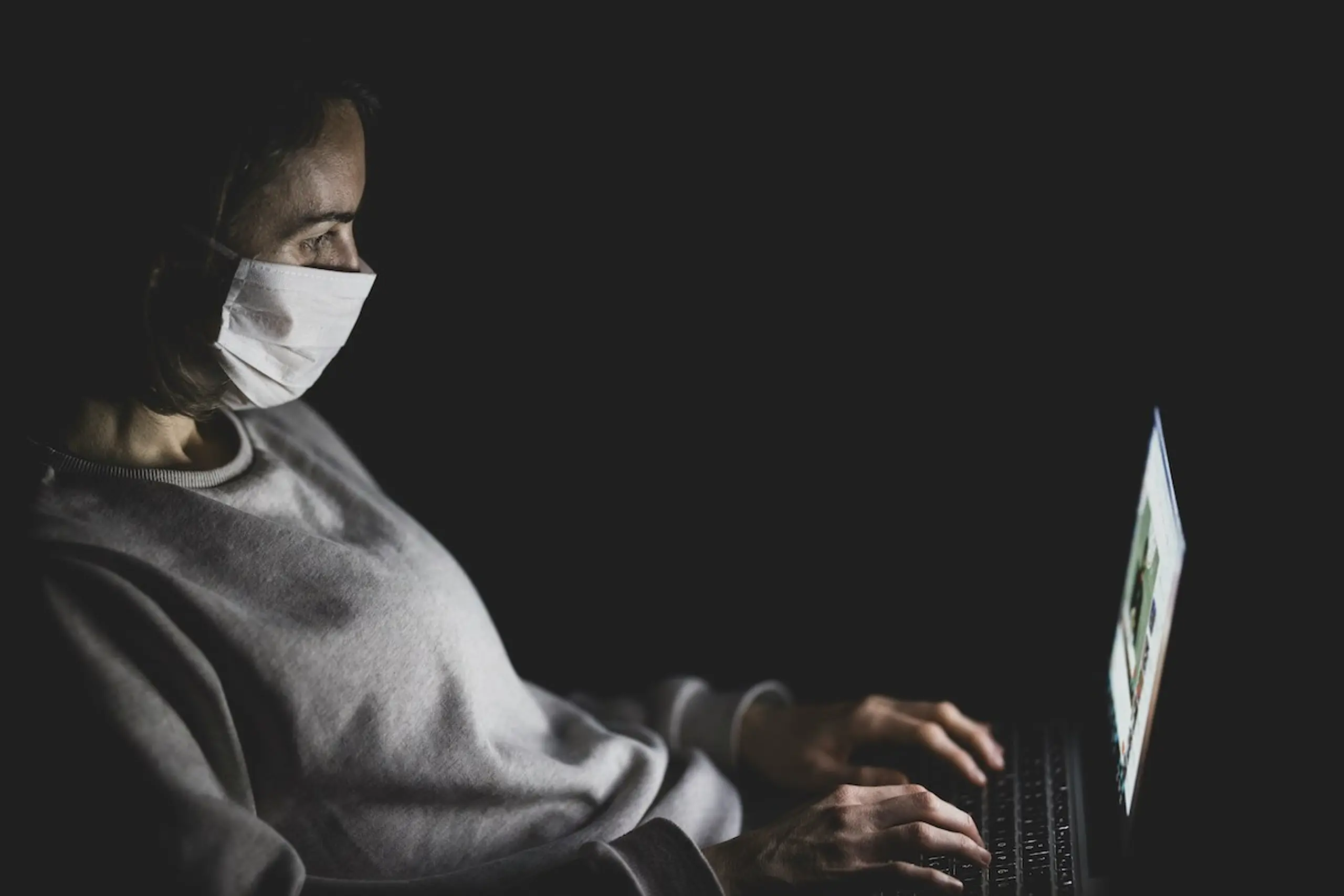 A woman wearing a mask while typing on the computer