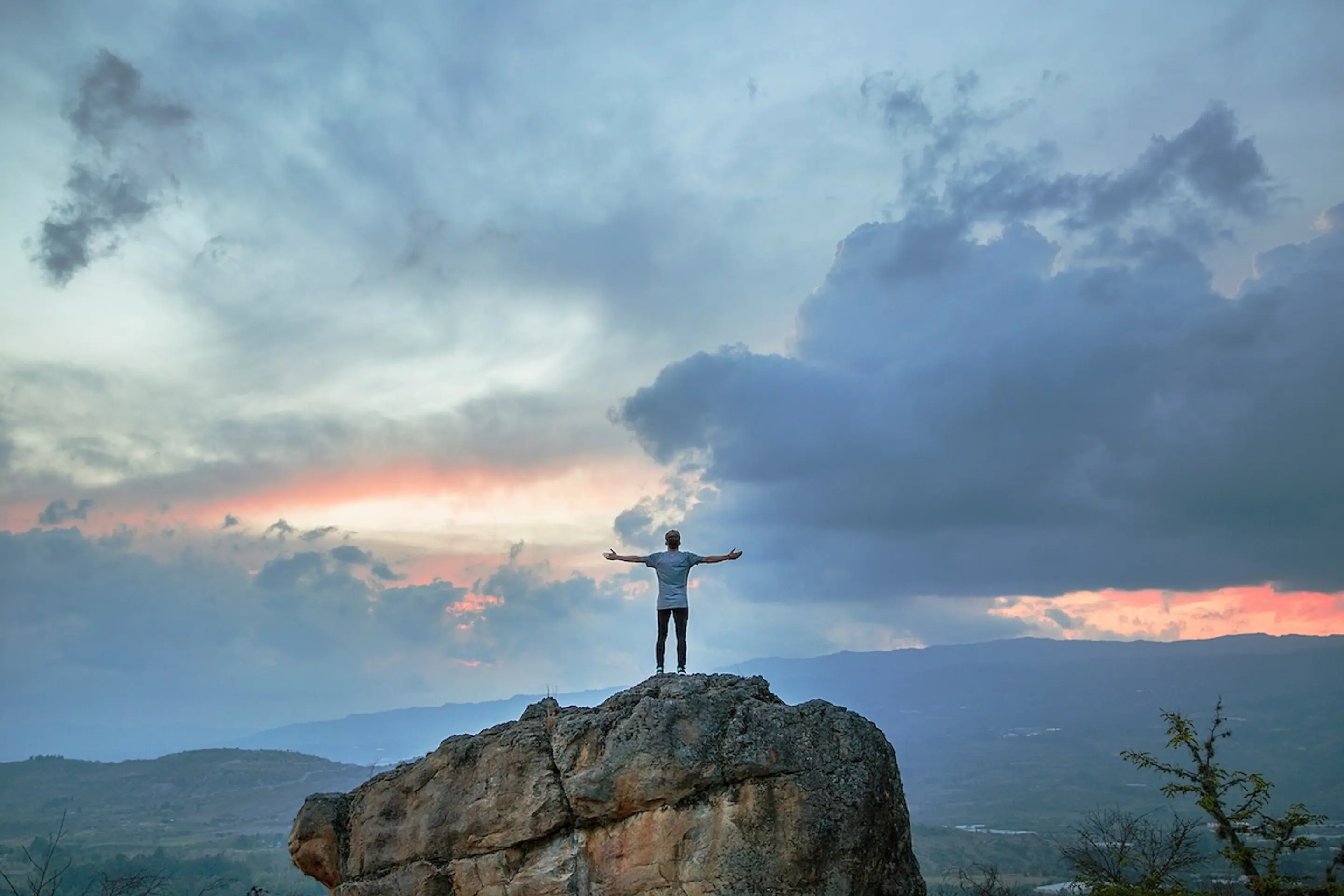 man on top of mountain looking at sky with arms open