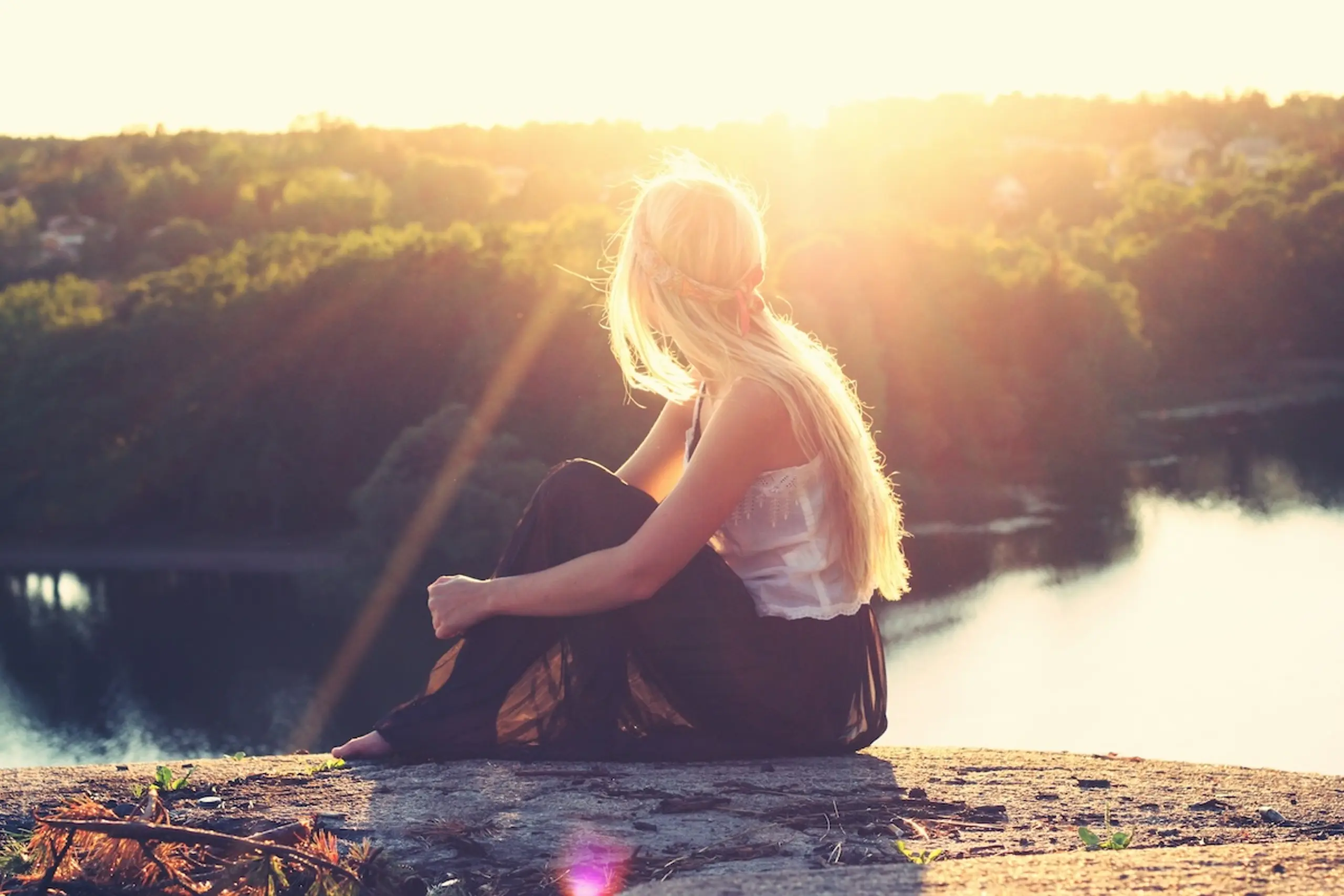 woman sitting on rock next to water and trees
