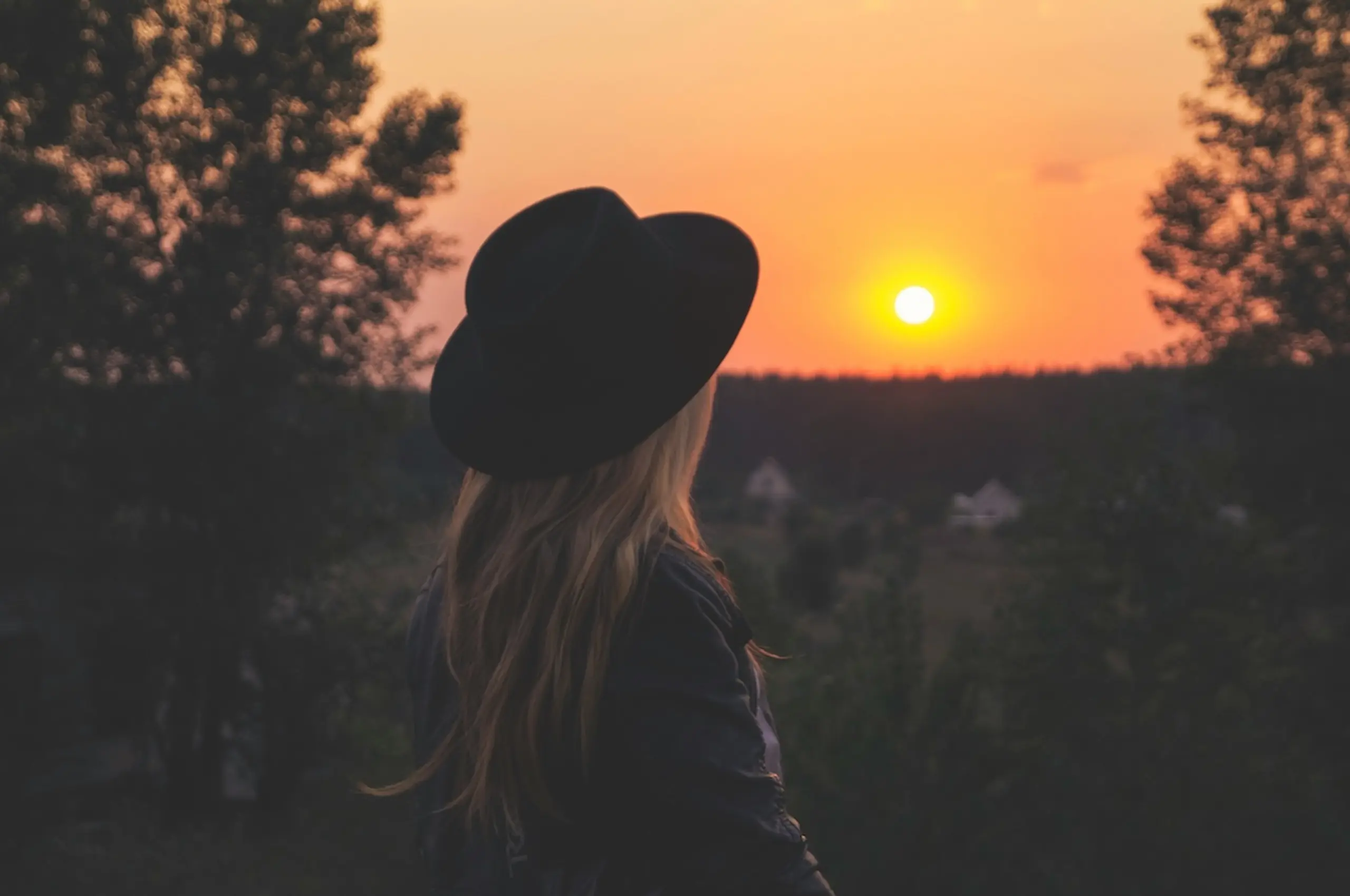 woman looking at sunset in the distance wearing a black flat brim hat