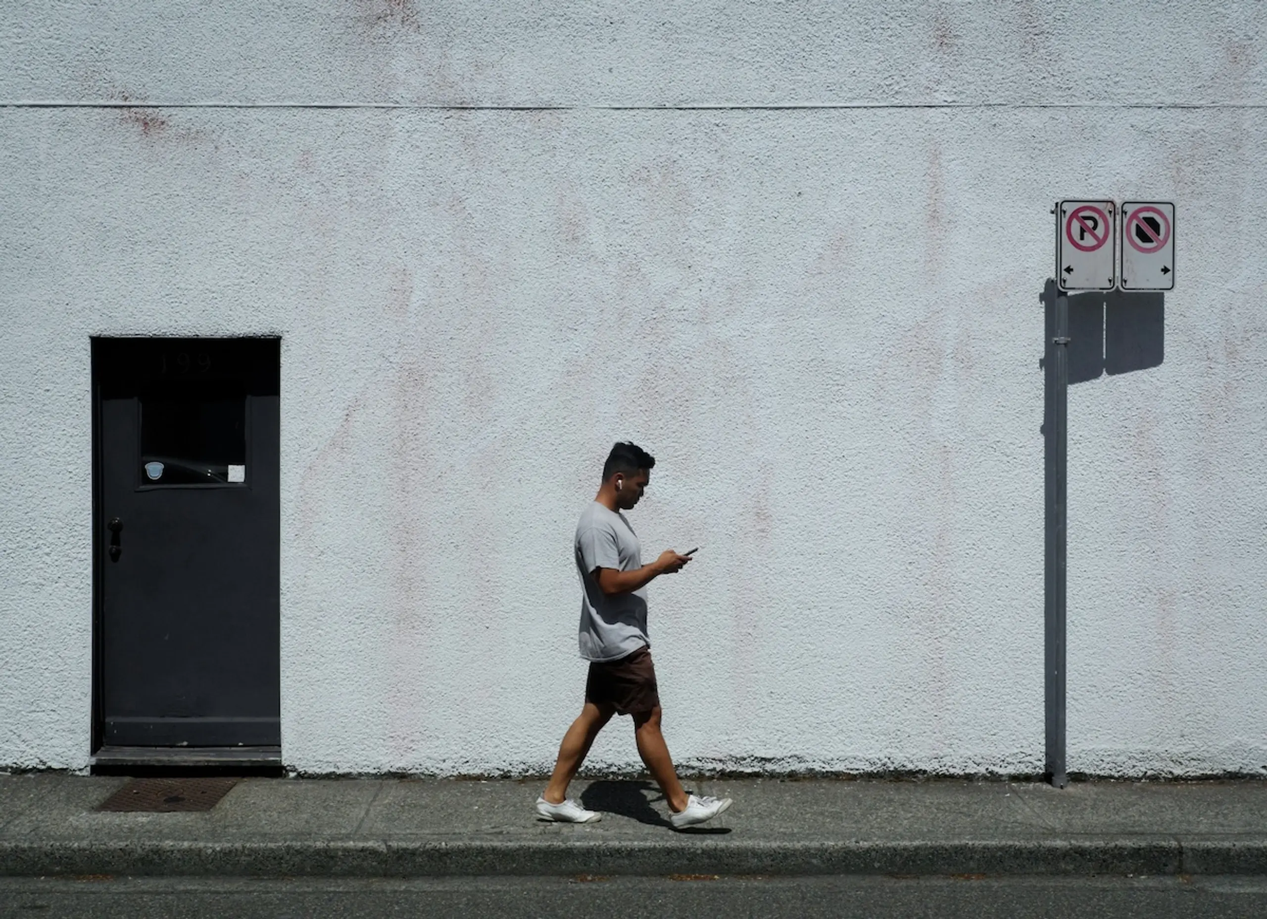 man walking down sidewalk looking at phone next to white building