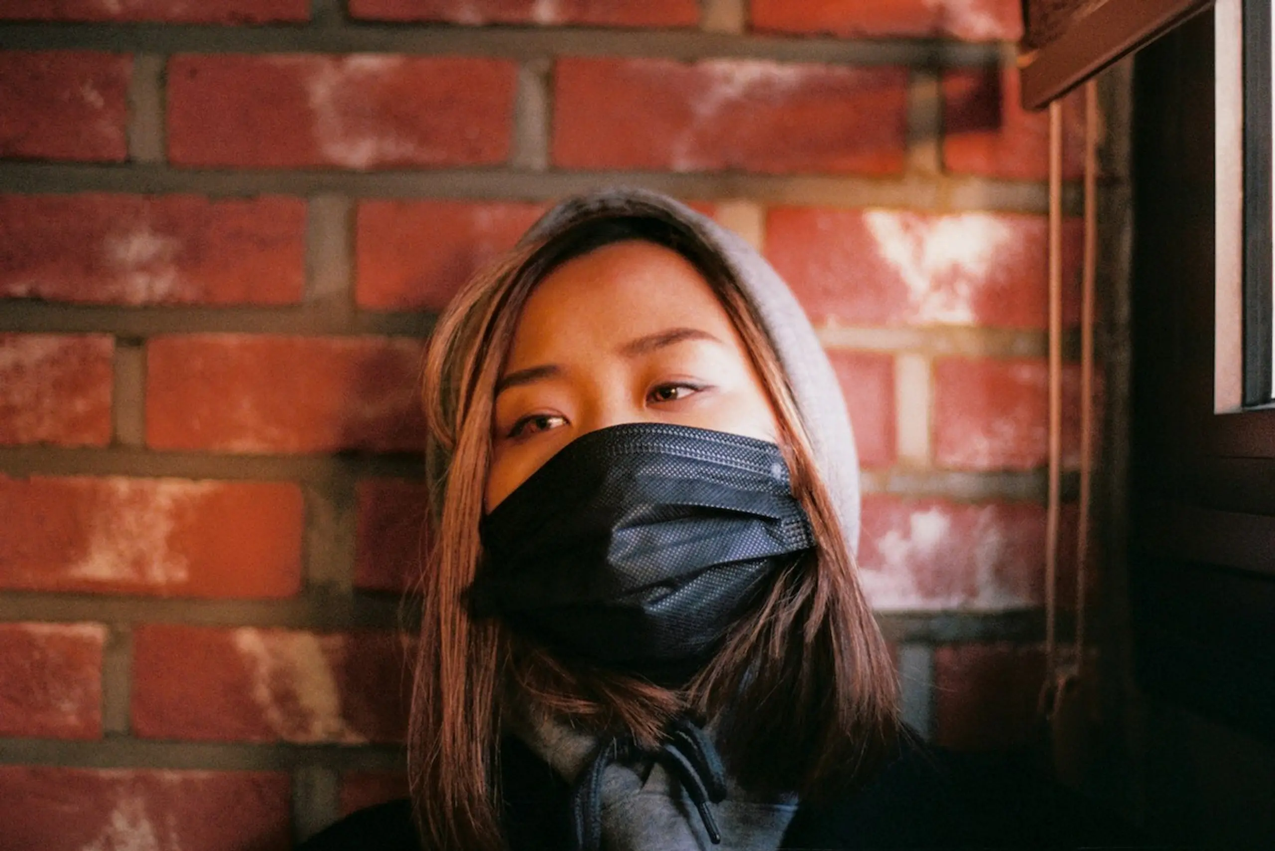 A woman with a mask leaning on a brick wall