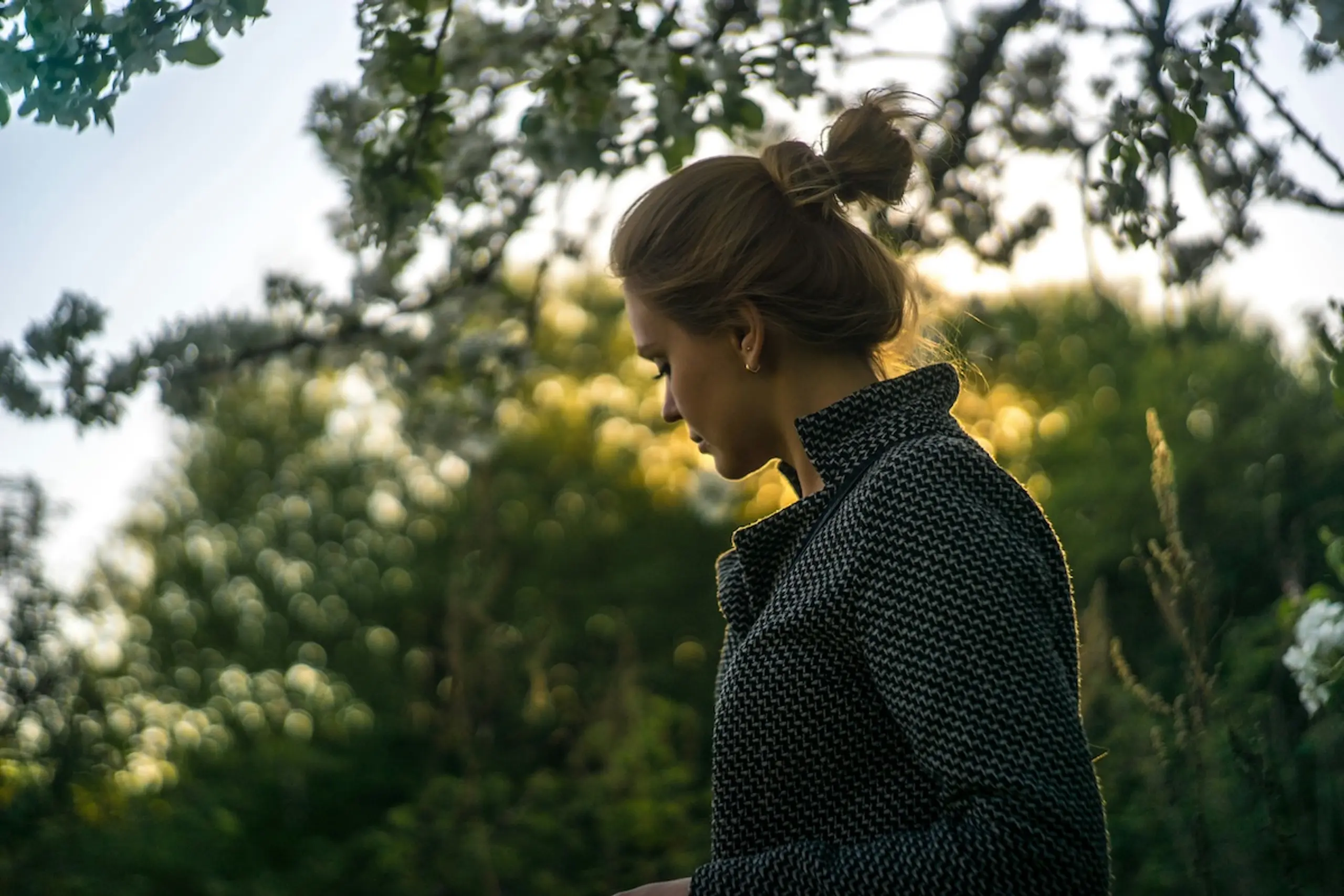woman standing among trees with her hair in a bun wearing a jacket