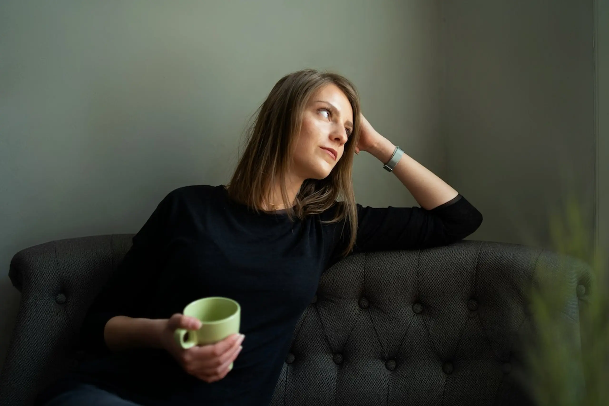 A woman thinking on the couch with a cup of tea