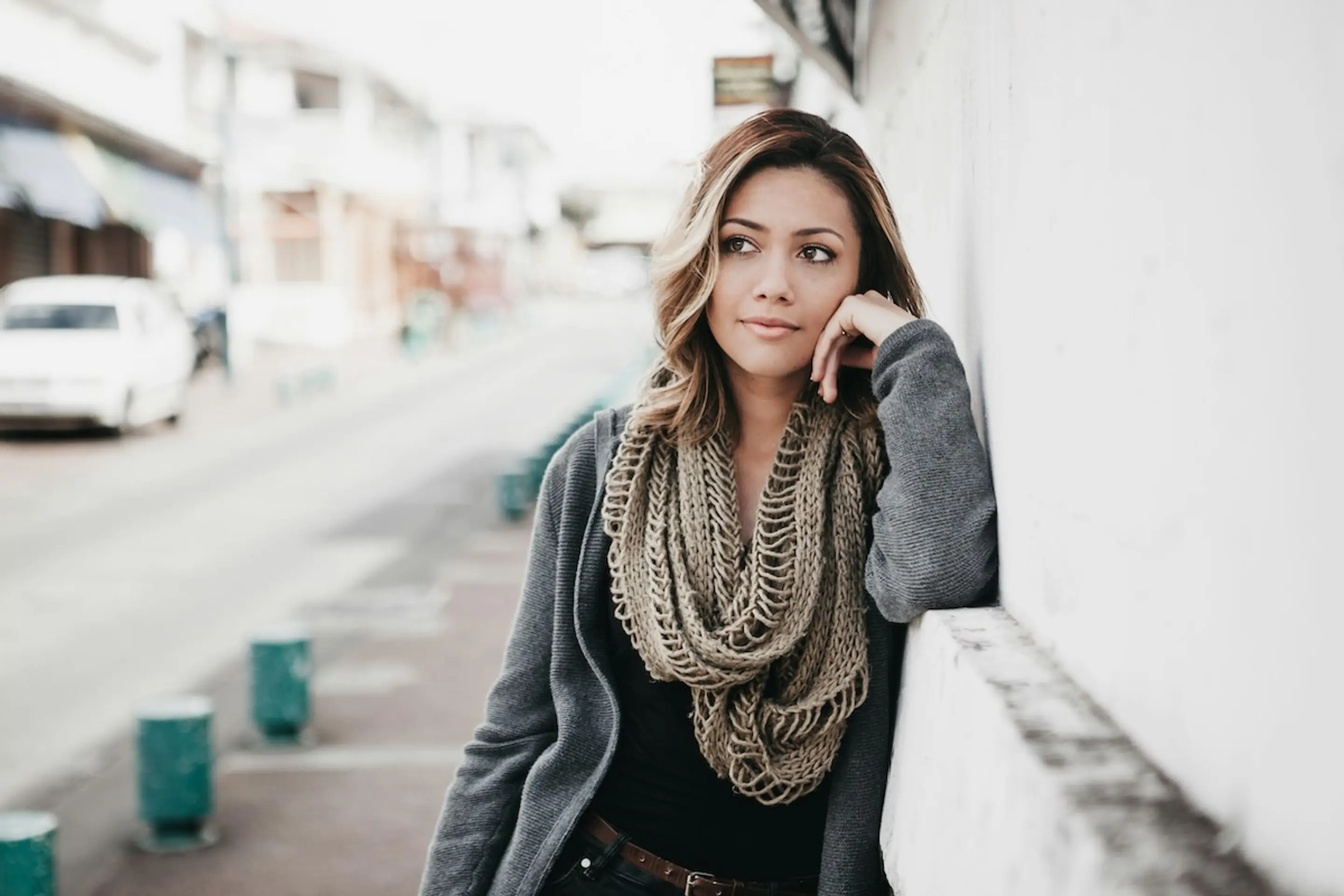 A woman thinking while standing outside against a wall