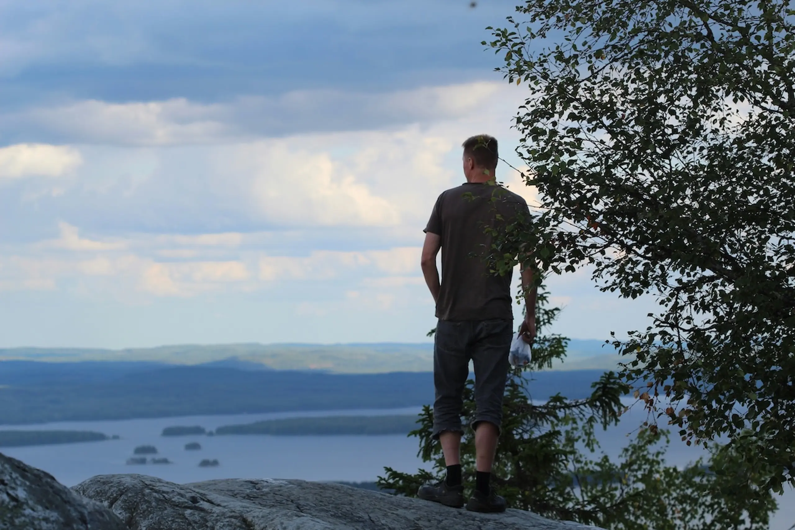a person looking out from a mountain peak onto water and rocks in the distance