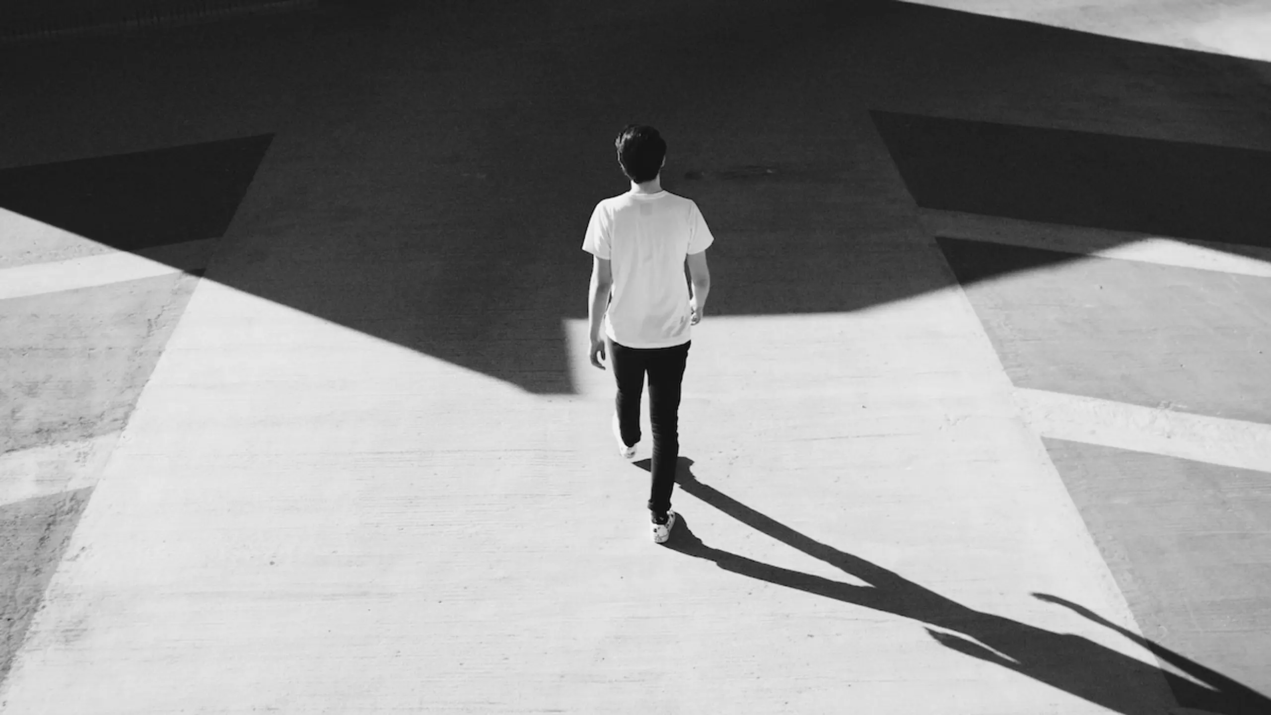 black and white photo of a man walking along a sidewalk with a shadow