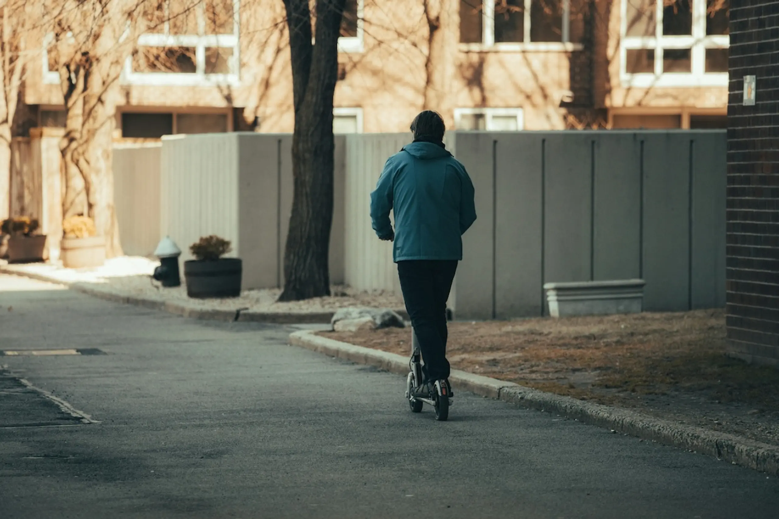 person riding scooter down neighborhood street in hat and jacket
